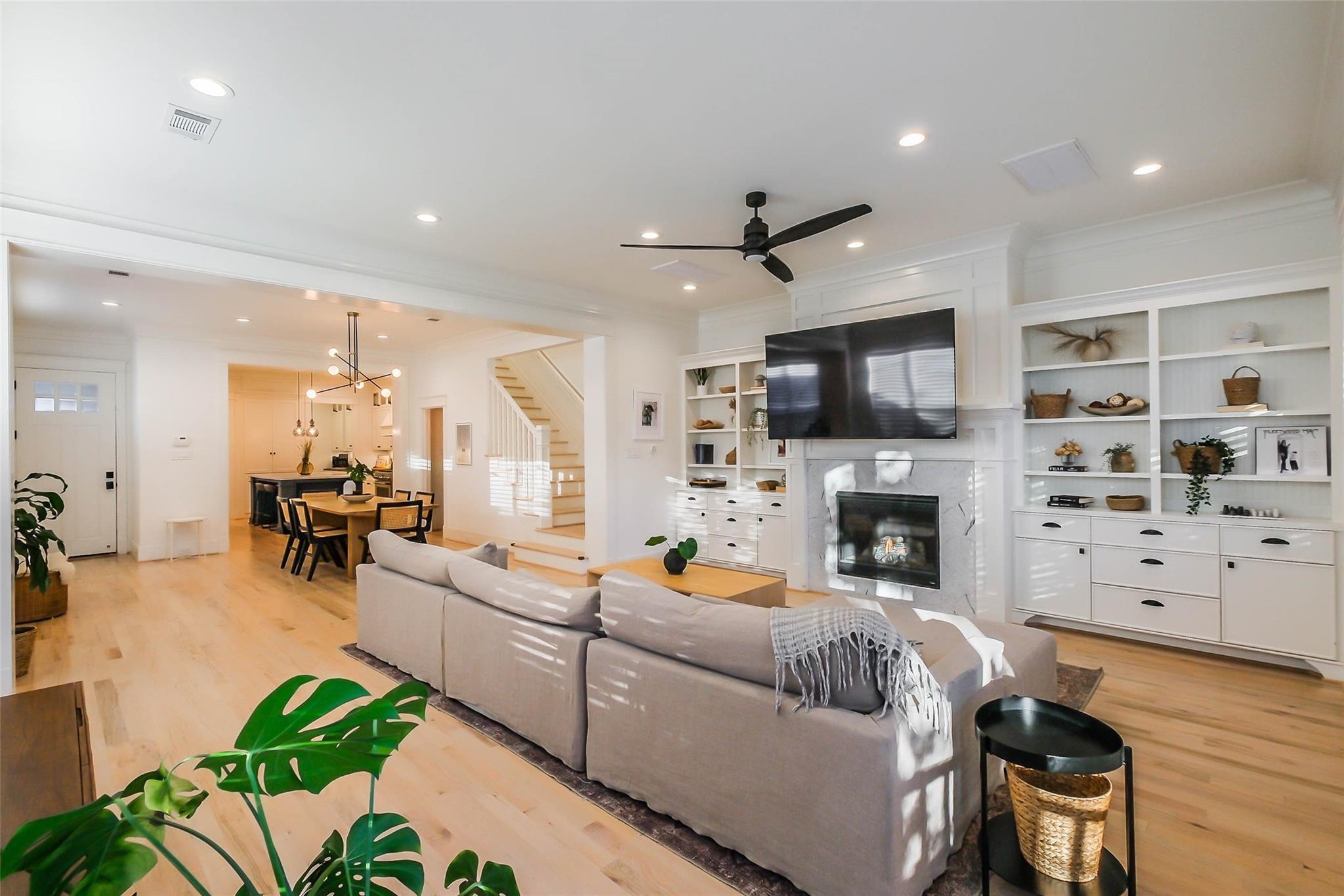 Open-plan living room with a gray sectional, built-in shelving, marble fireplace, and dining area beyond.