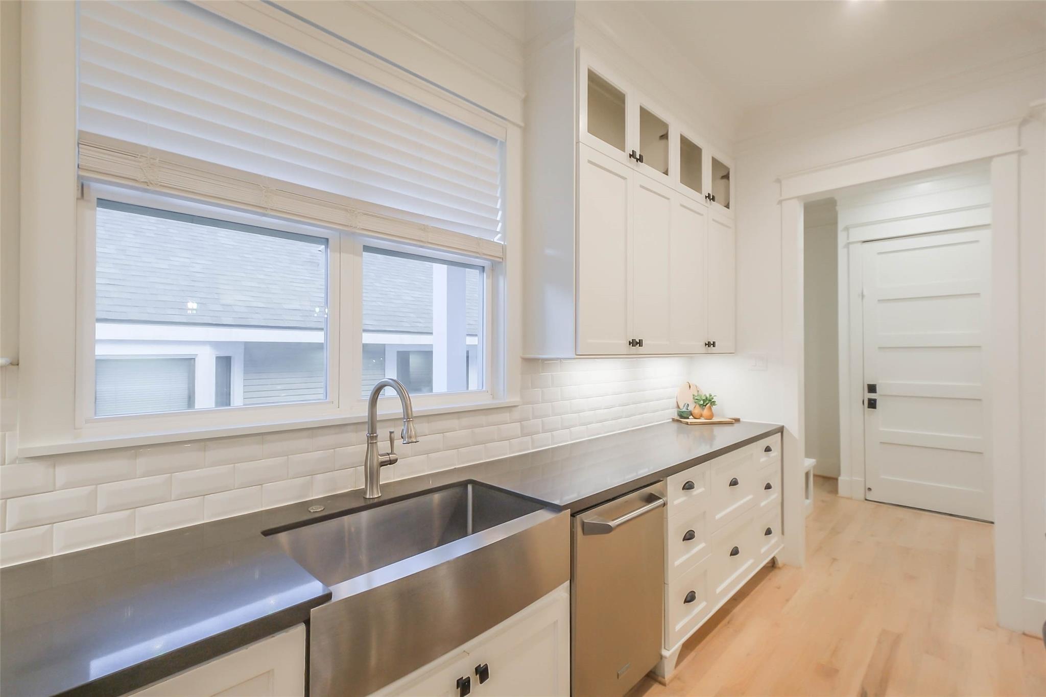 Bright kitchen with white cabinetry, stainless farmhouse sink, subway tile backsplash, and light wood floors.
