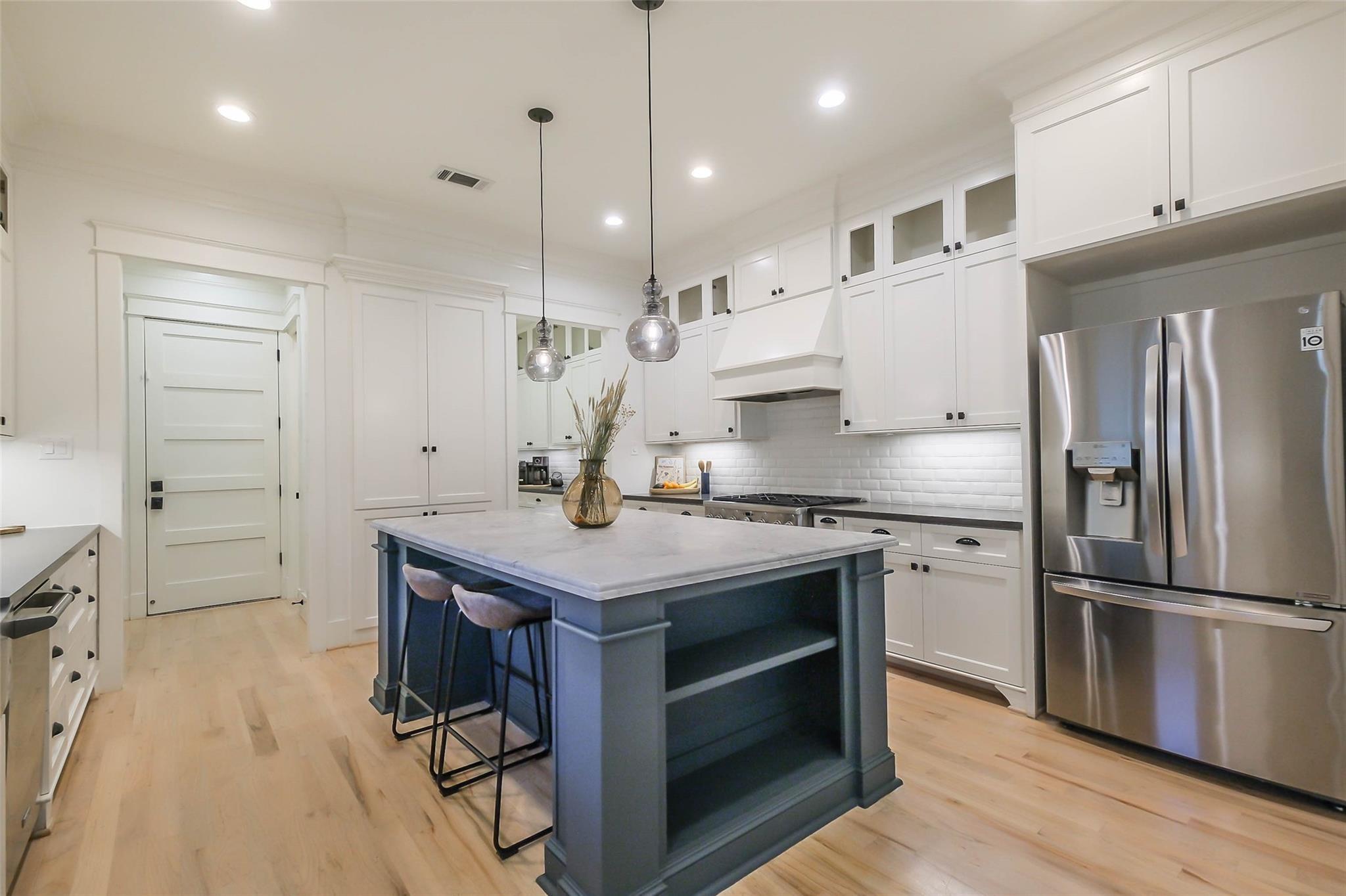 Bright kitchen with a blue-gray island, white cabinetry, stainless steel appliances, and light wood floors.