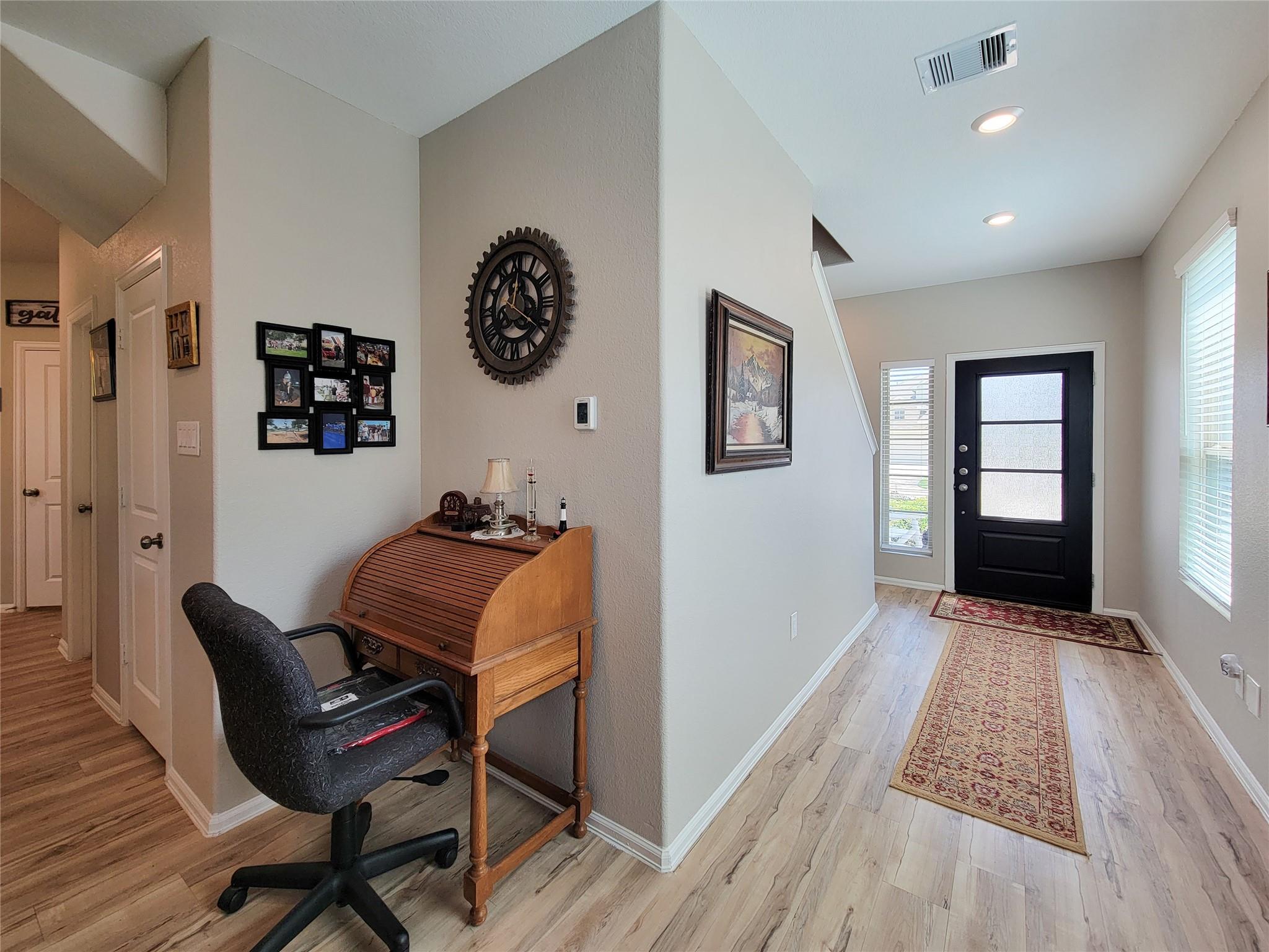 Furnished entryway with black front door, patterned rugs, and a roll-top desk beside a chair.
