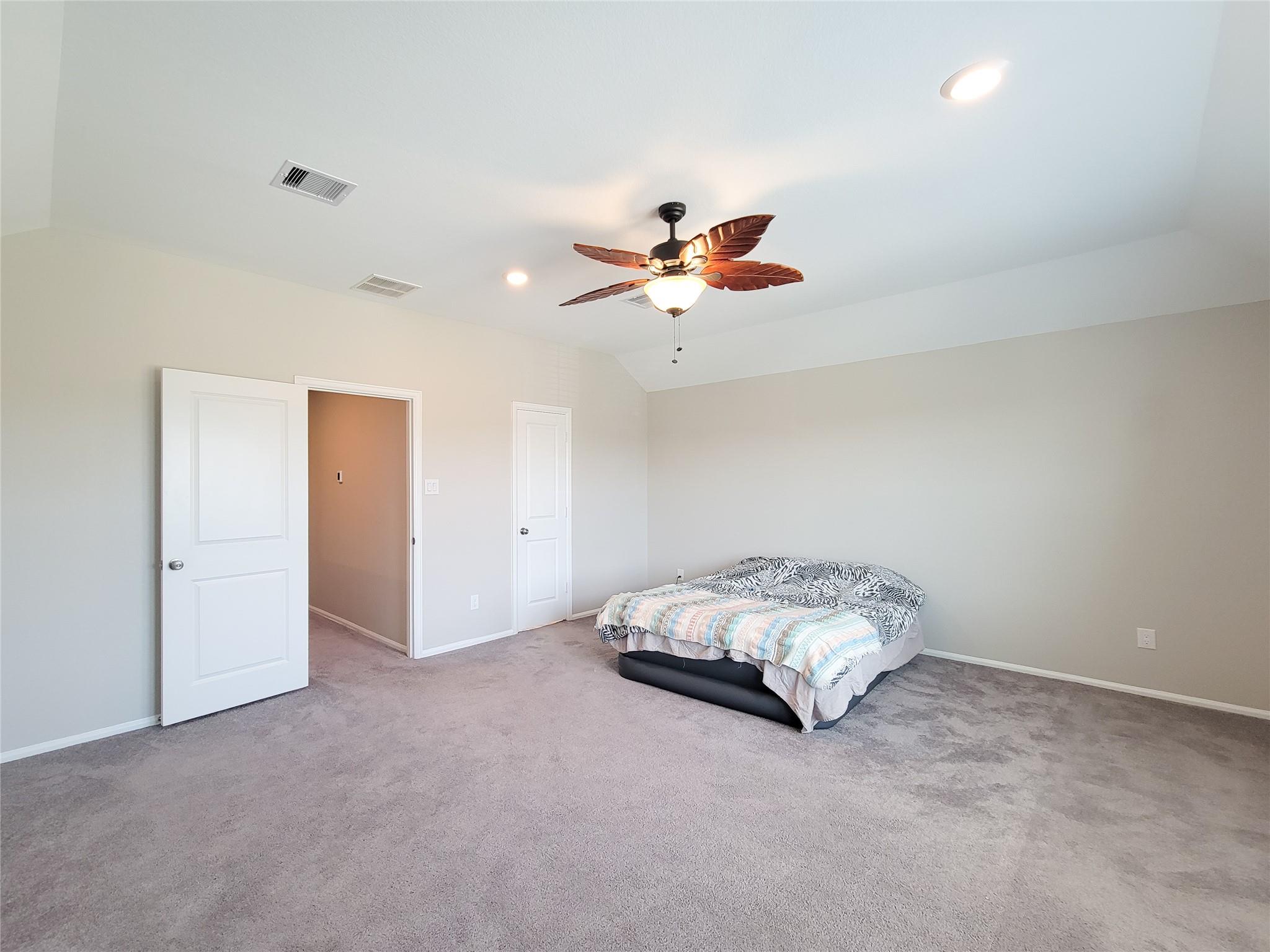 Bedroom with gray carpet, a bed with patterned bedding, and a leaf-shaped ceiling fan.