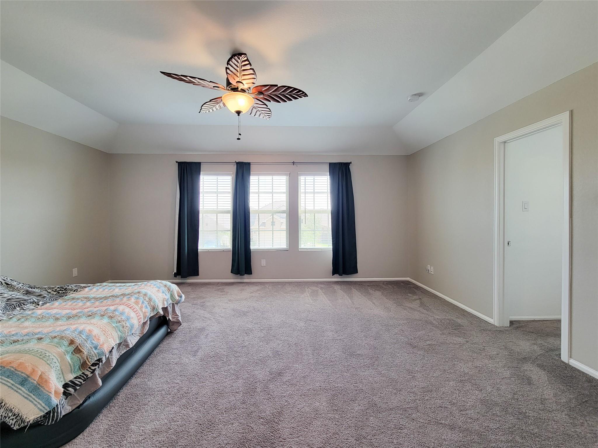 Carpeted bedroom with three curtained windows and a leaf-shaped ceiling fan.