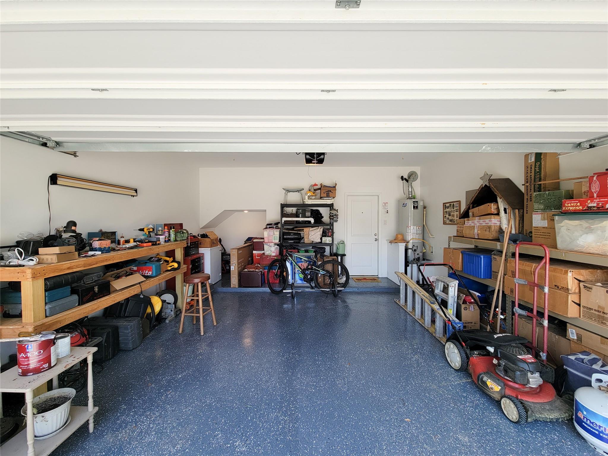 Garage with a blue speckled floor, workbench, bicycles, boxes, and lawn mower.
