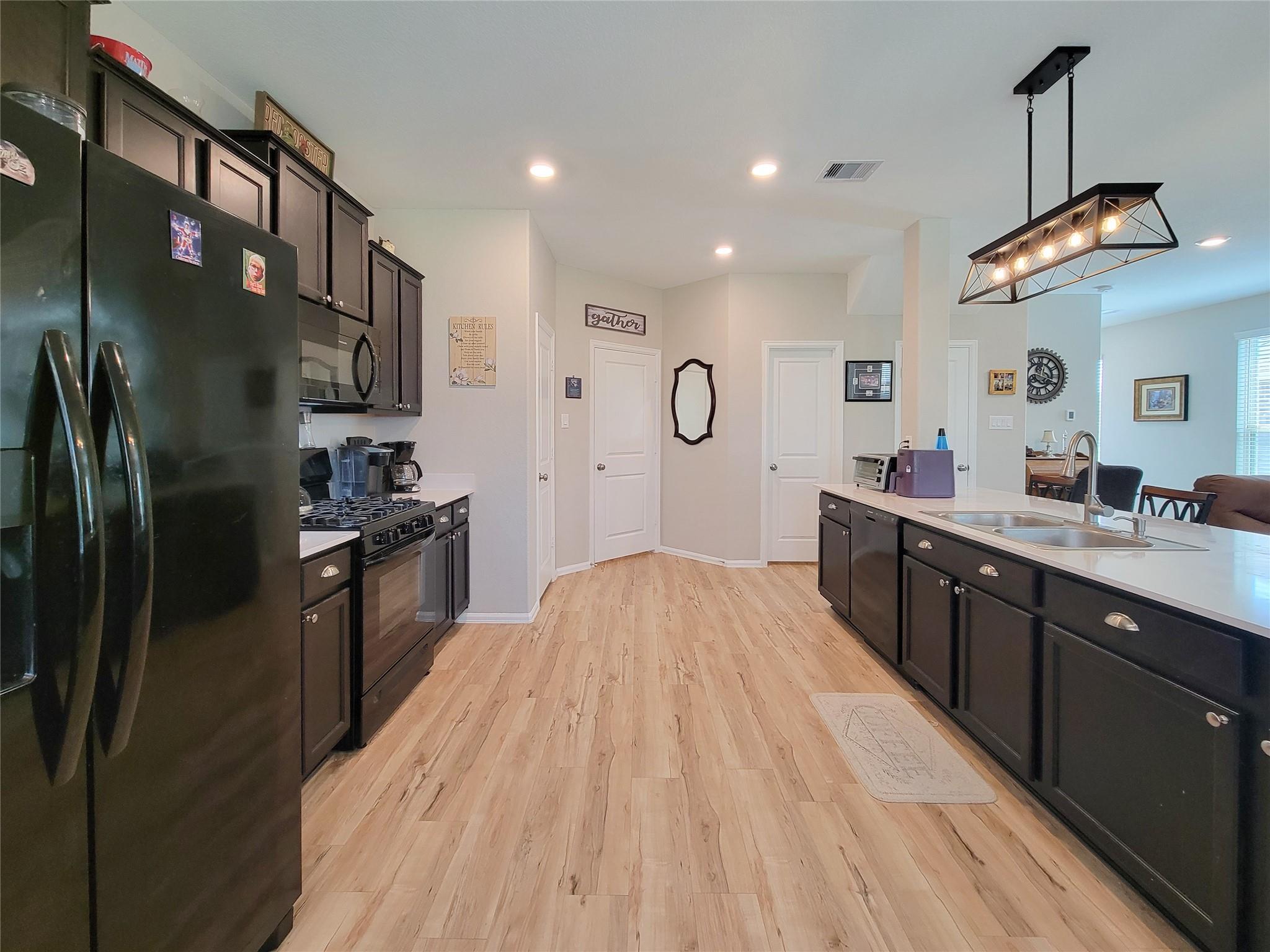 Kitchen with dark cabinets, a large sink island, and a geometric pendant light.