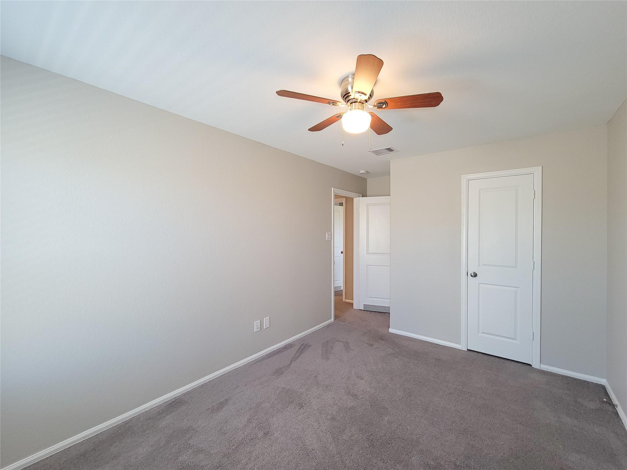 Empty bedroom with gray carpet, a ceiling fan, and white paneled doors.