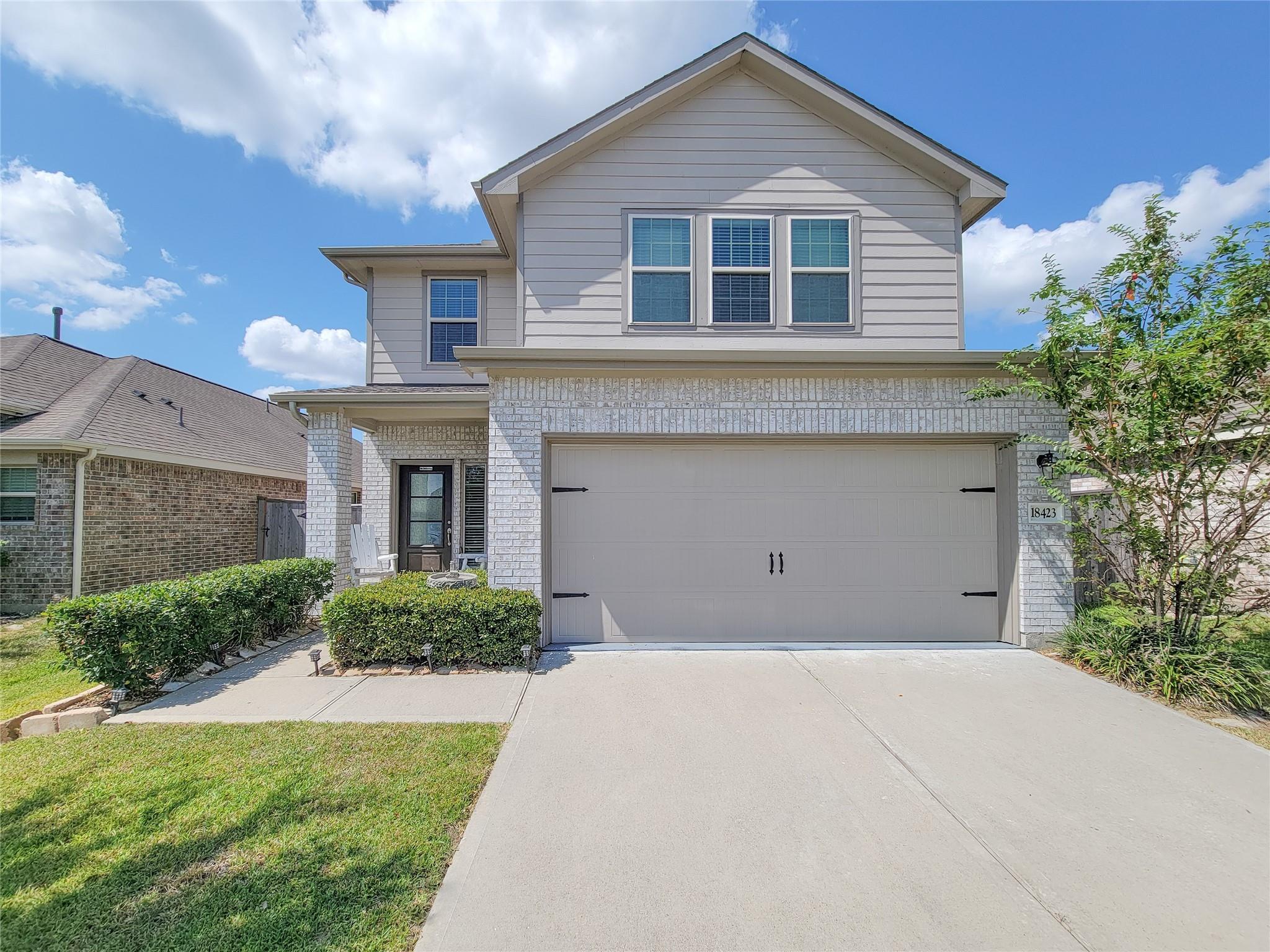 Two-story house with light brick, gray siding, a double garage, and a wide concrete driveway.