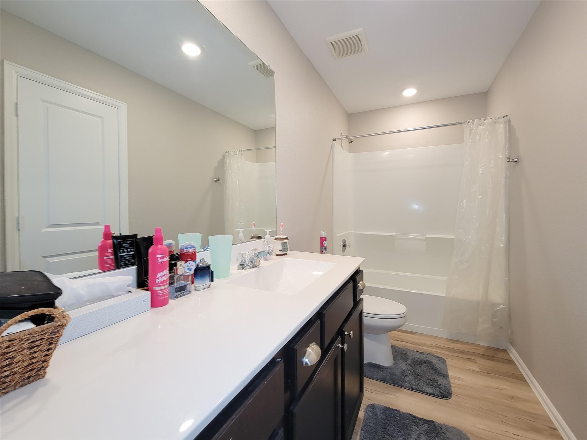 Bathroom with a long white vanity, large mirror, and tub-shower with a curtain.