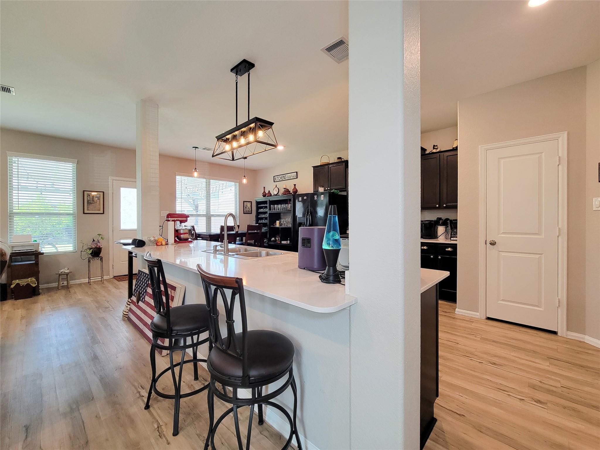 Open kitchen with a white breakfast-bar island, dark cabinets, and wood floors.