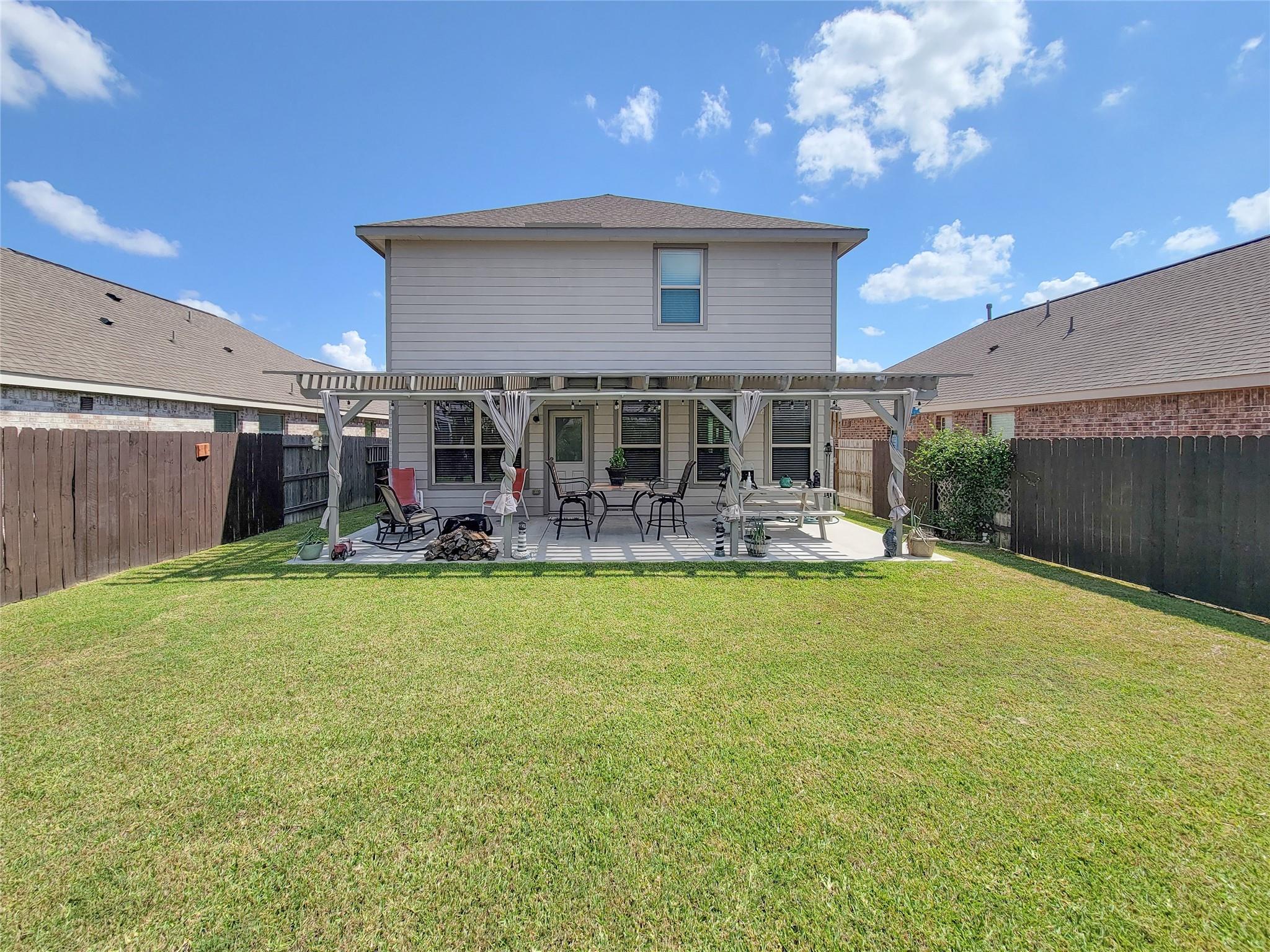 Two-story gray house with a covered, furnished patio overlooking a broad fenced lawn.