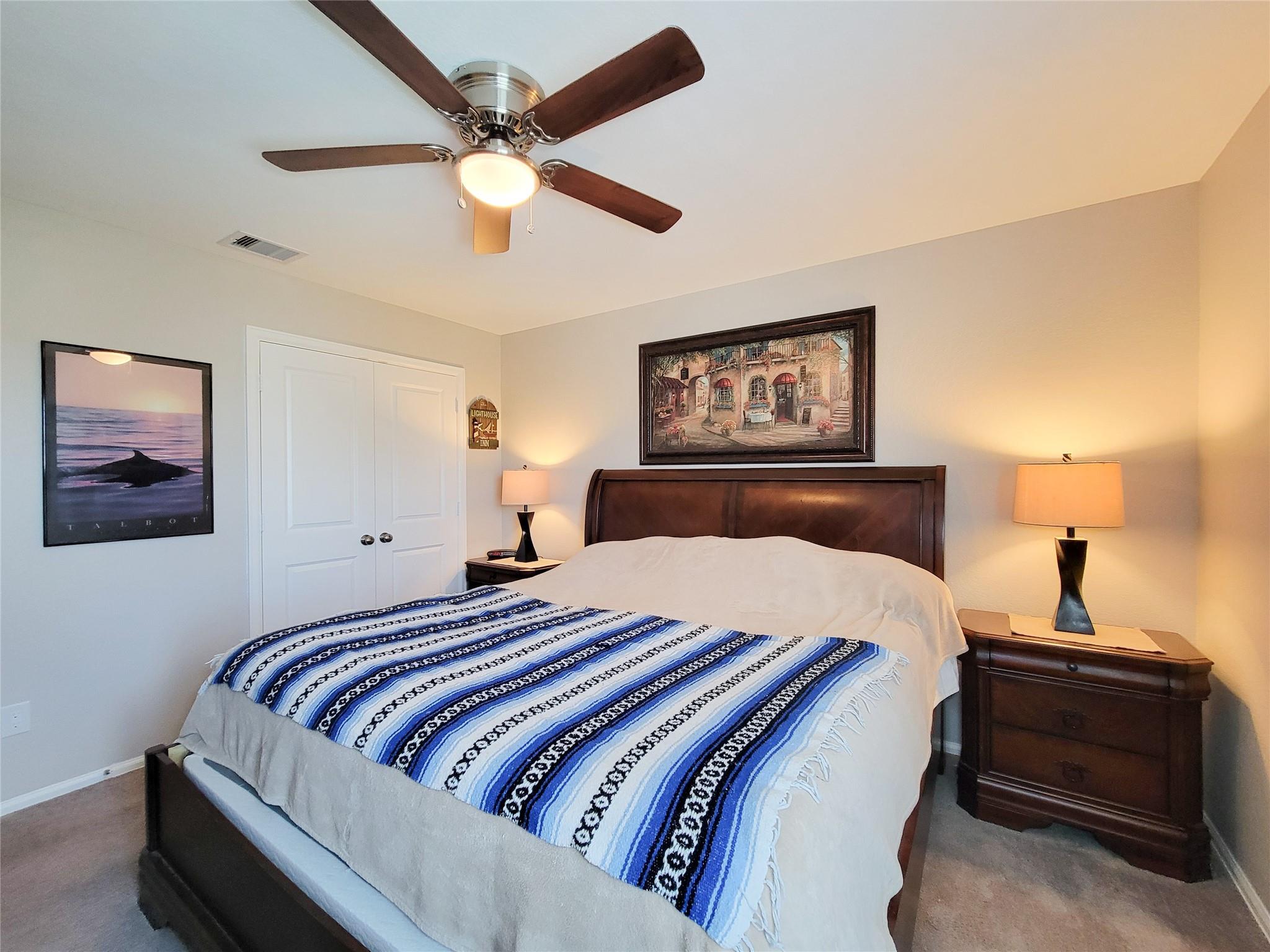 Bedroom with a dark wood bed, blue-and-white striped blanket, and ceiling fan.
