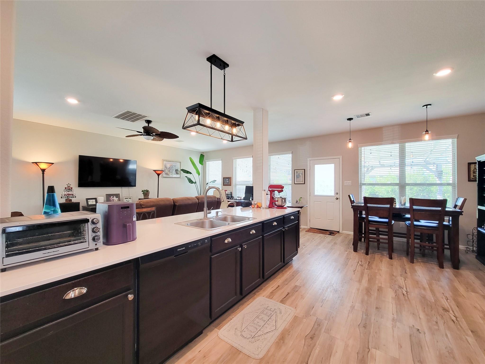 Open kitchen with a long white island, dark cabinets, double sink, and adjoining dining area.