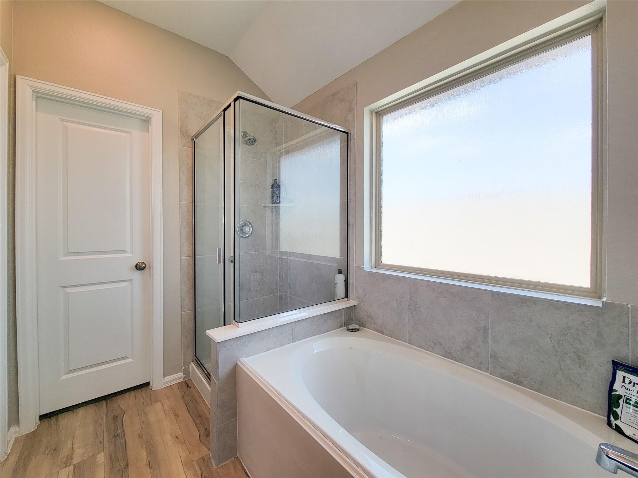 Bathroom with a built-in tub, glass-enclosed shower, gray tile, and a large frosted window.