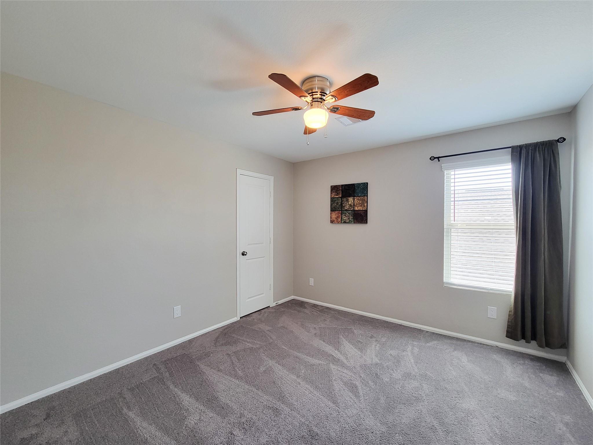 Empty bedroom with gray carpet, ceiling fan, and a curtained window.