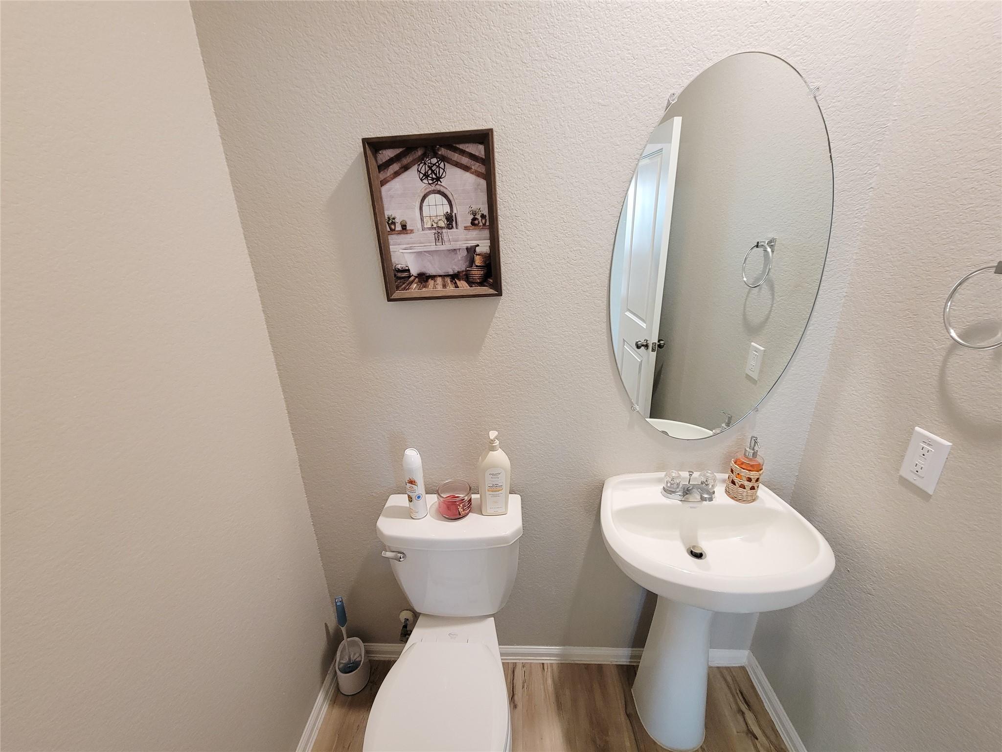 Powder room with a white toilet, pedestal sink, and large oval mirror.
