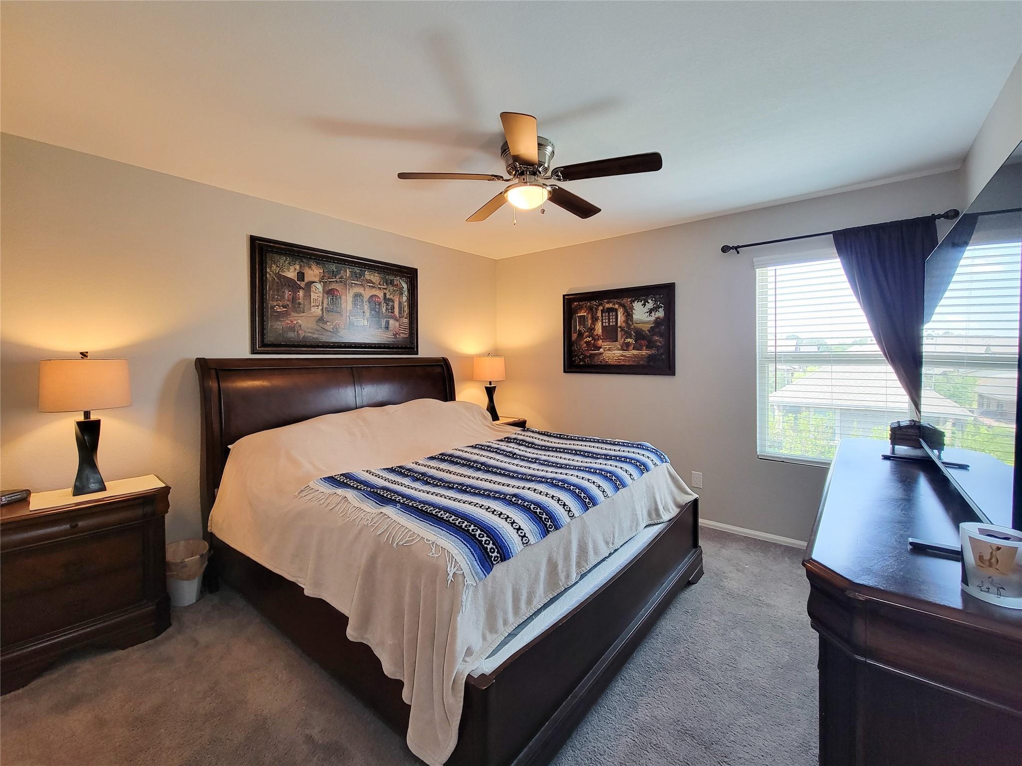 Furnished bedroom with a dark wood bed, blue patterned throw, and large curtained window.