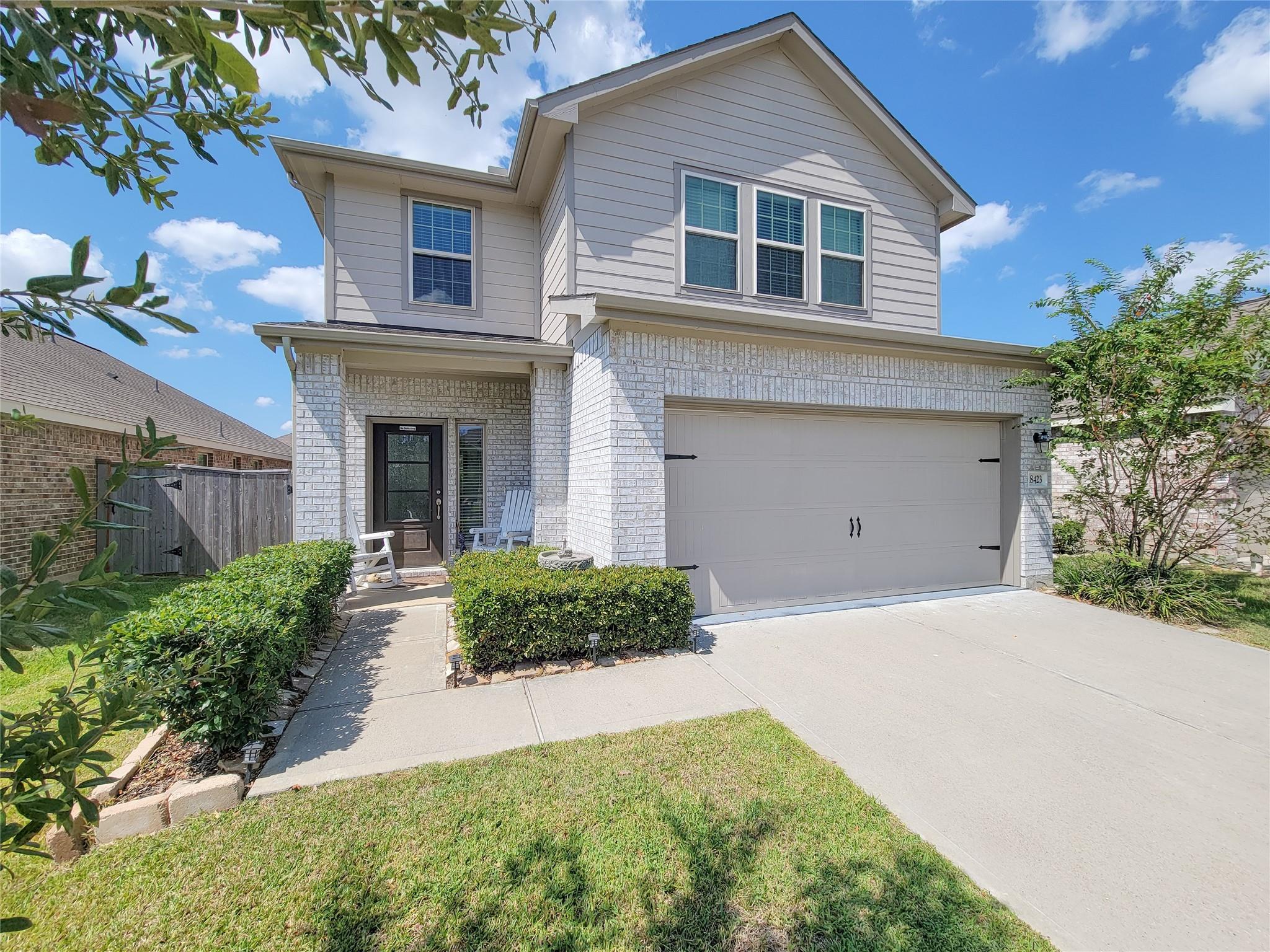 Two-story gray-sided and white-brick house with a double garage, covered entry, and trimmed front hedges.