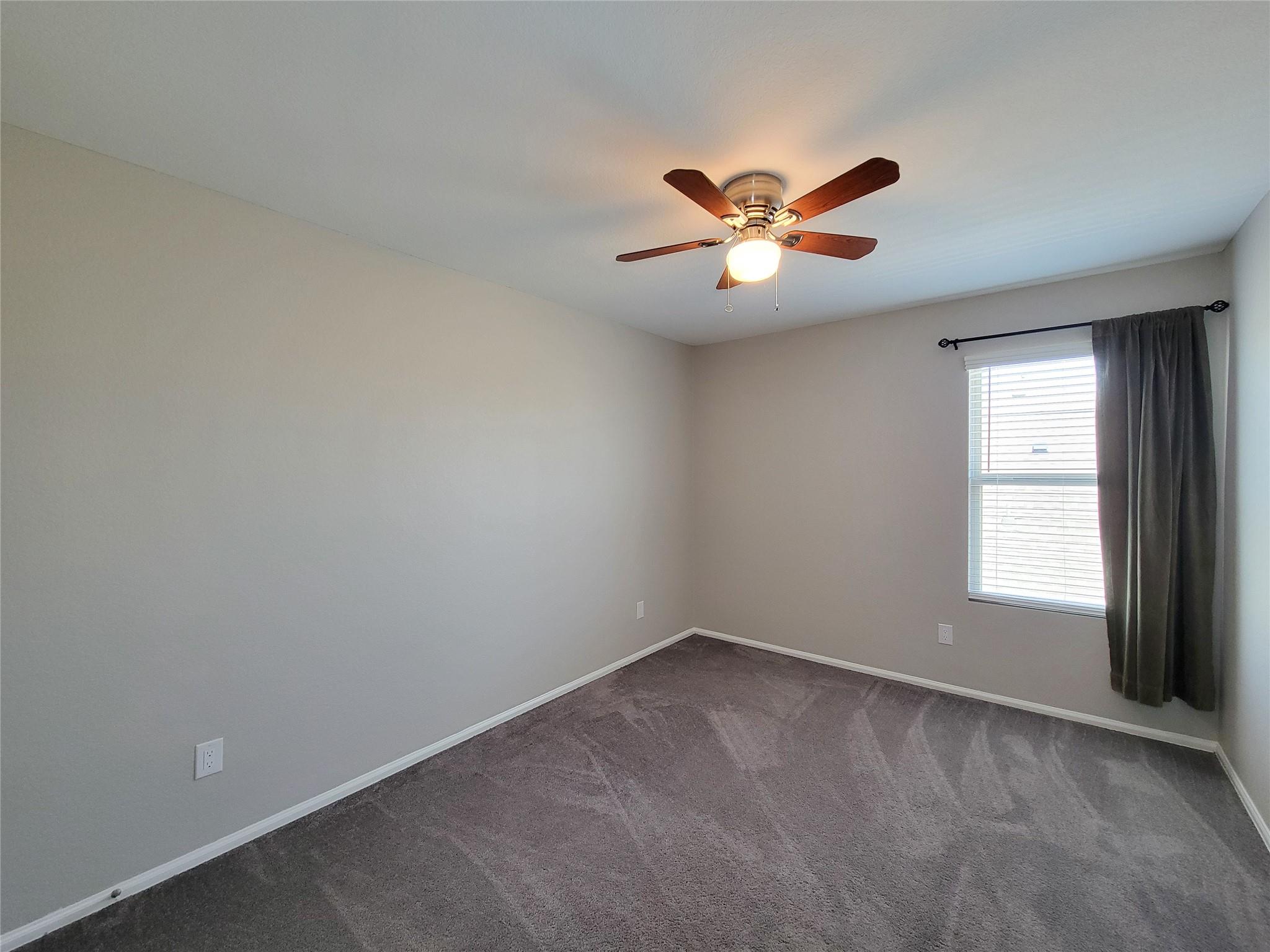 Empty carpeted bedroom with a ceiling fan and a curtained window.