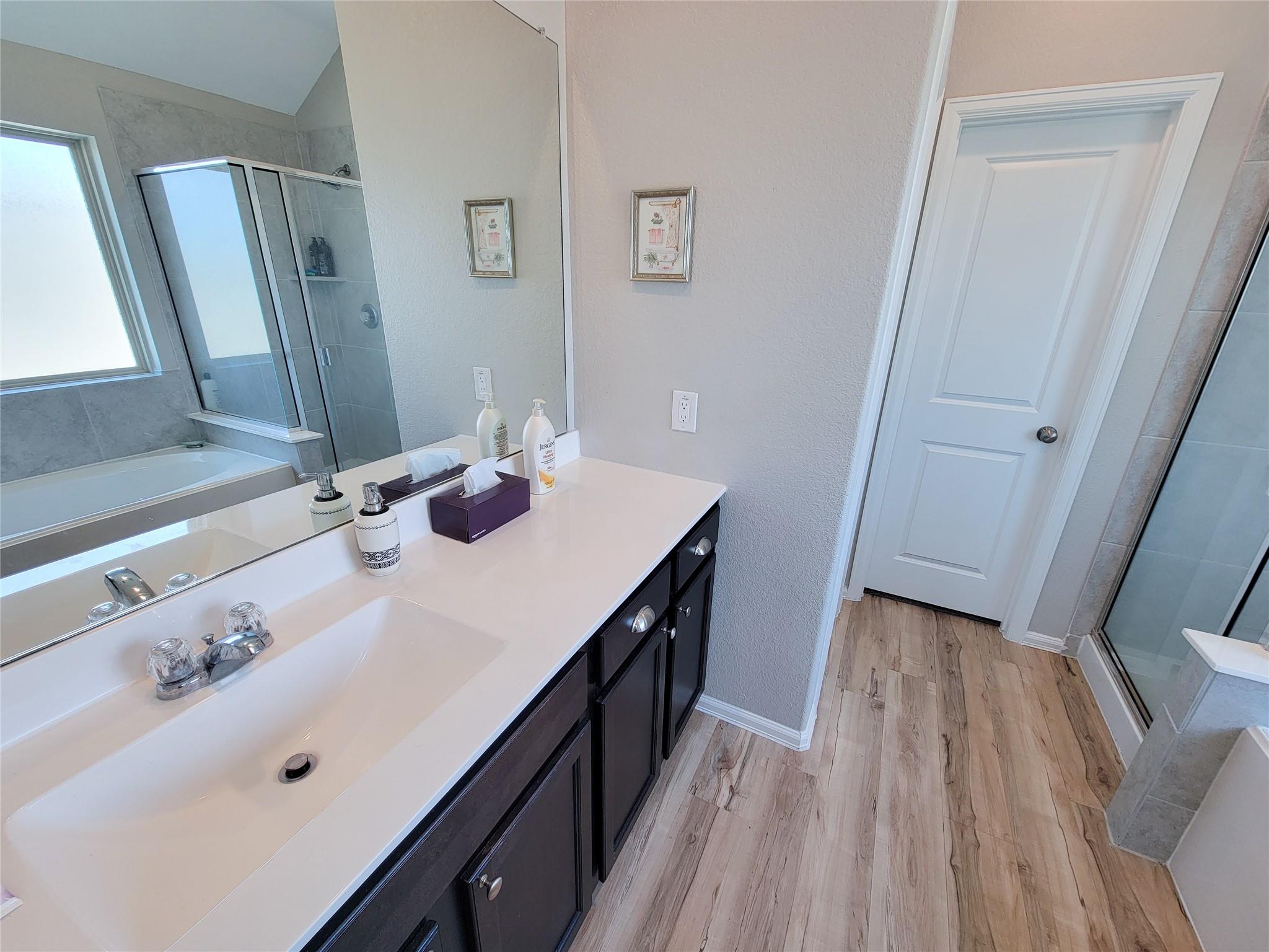 Bathroom with a long dark vanity, double sinks, bathtub, and glass-enclosed shower.