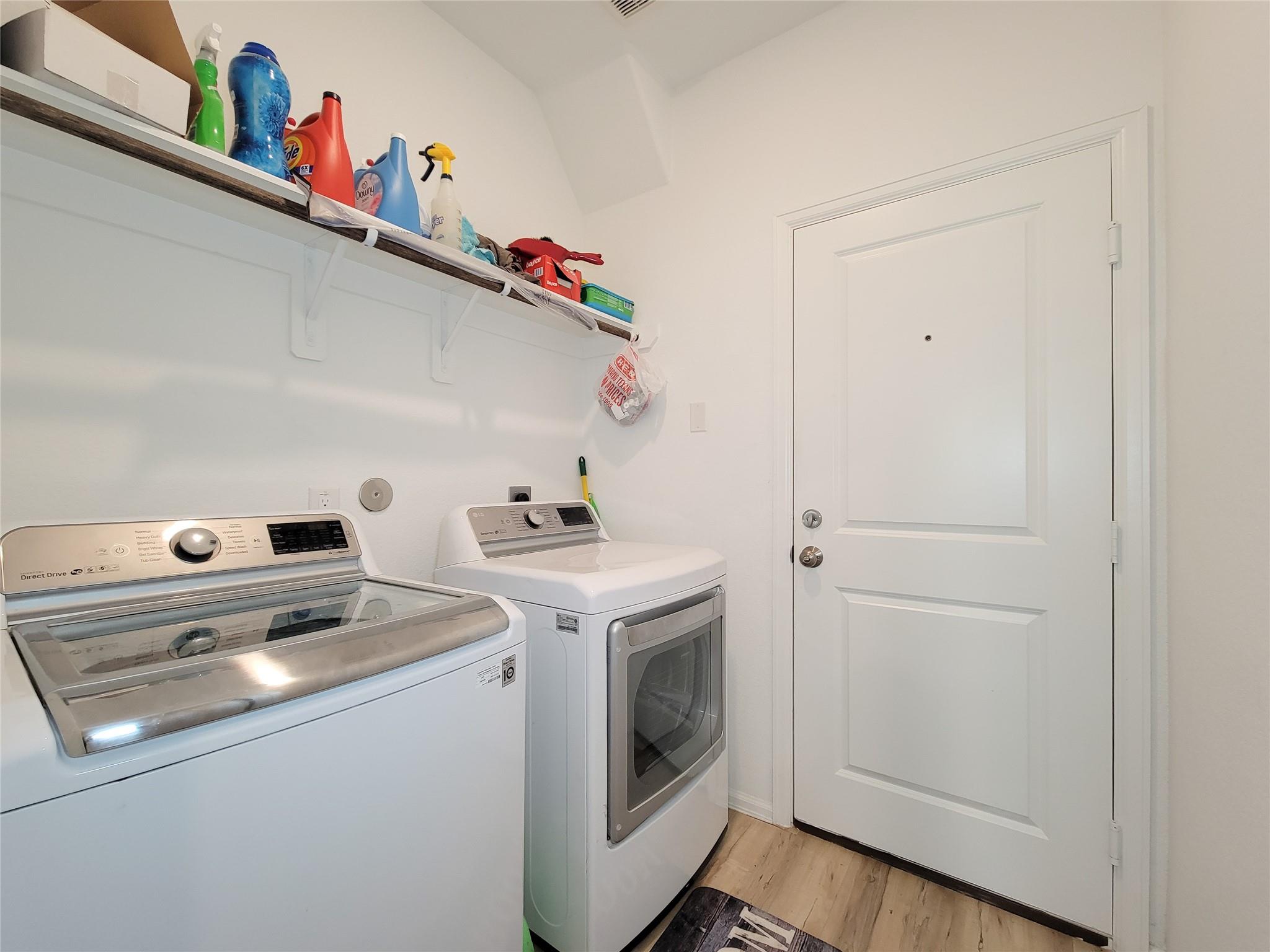 Laundry room with a washer and dryer beneath an open shelf of cleaning supplies.