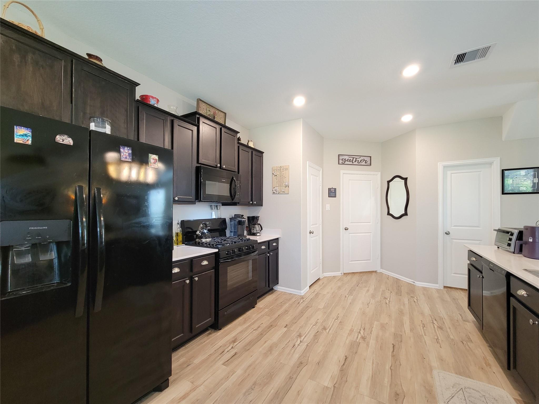 Kitchen with dark cabinets and black appliances, opening onto a light wood-look floor.