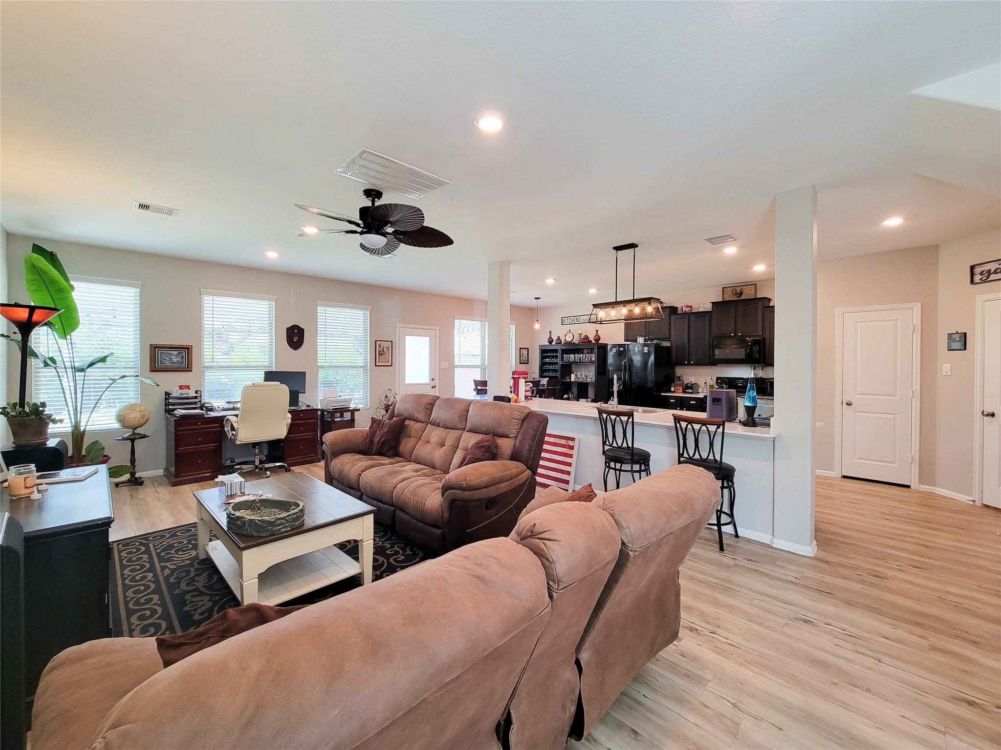 Open-plan living room with brown sofas, a desk area, and a kitchen breakfast bar.