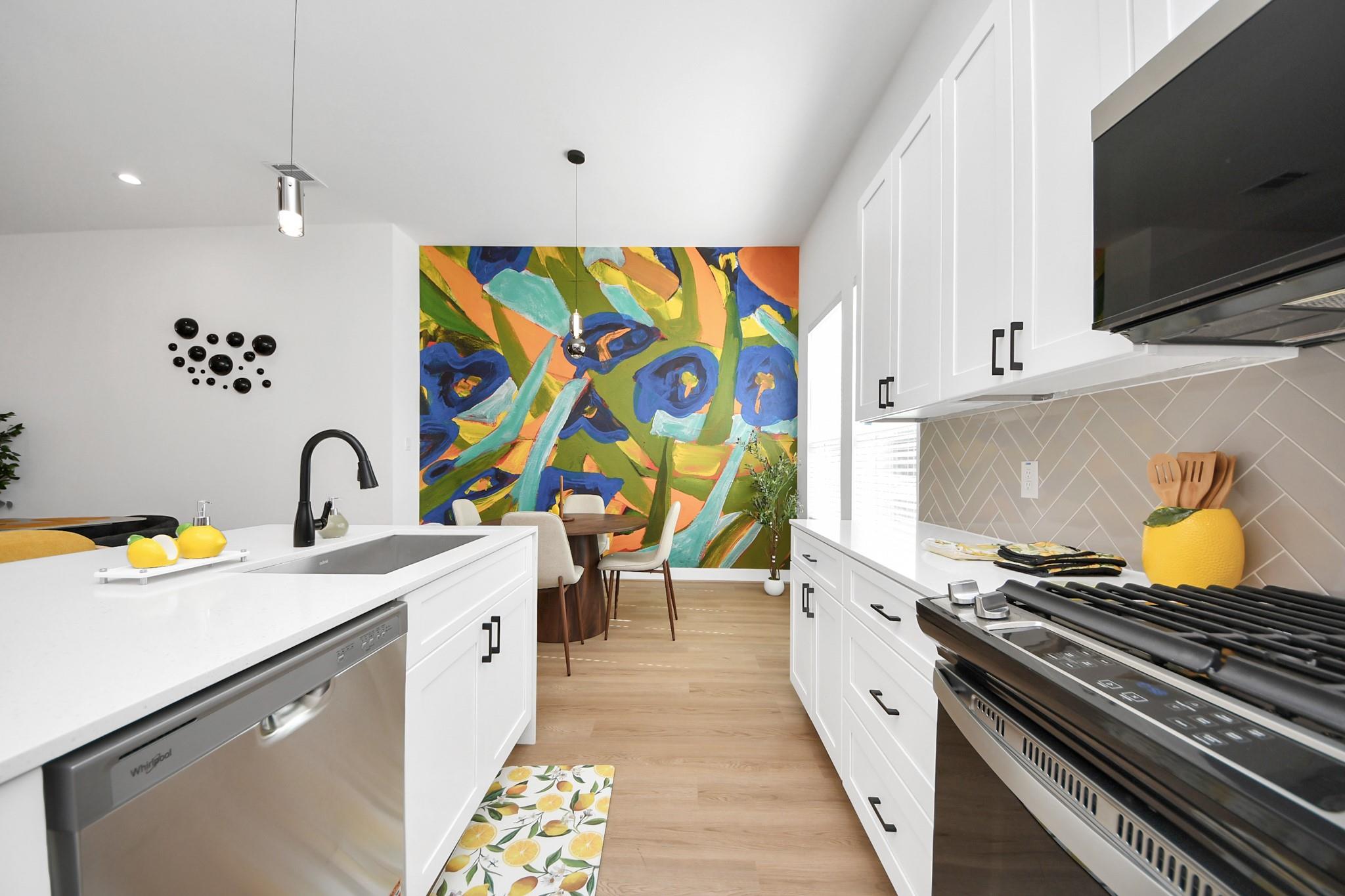 Modern white kitchen with a large colorful abstract mural behind the dining area.