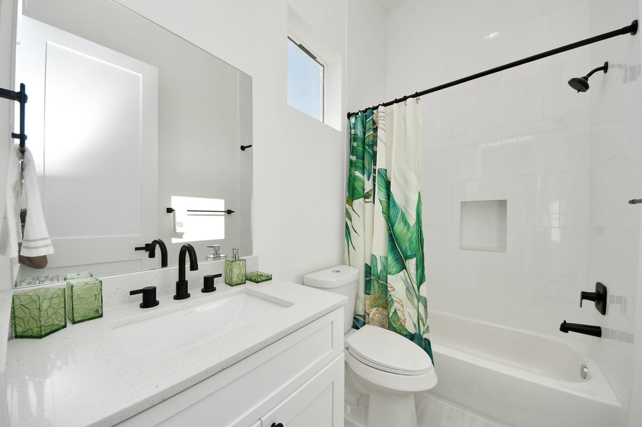 Bright bathroom with a white vanity, black fixtures, and a leaf-print shower curtain beside the tub.