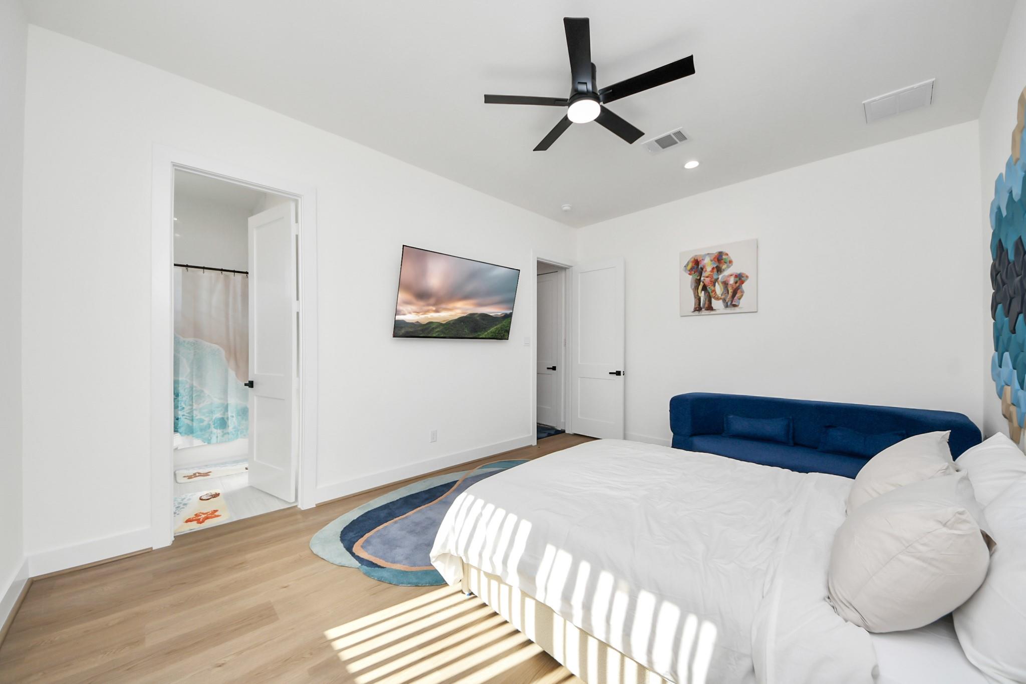 Bright bedroom with a white bed, blue headboard, and doorway to a bathroom.