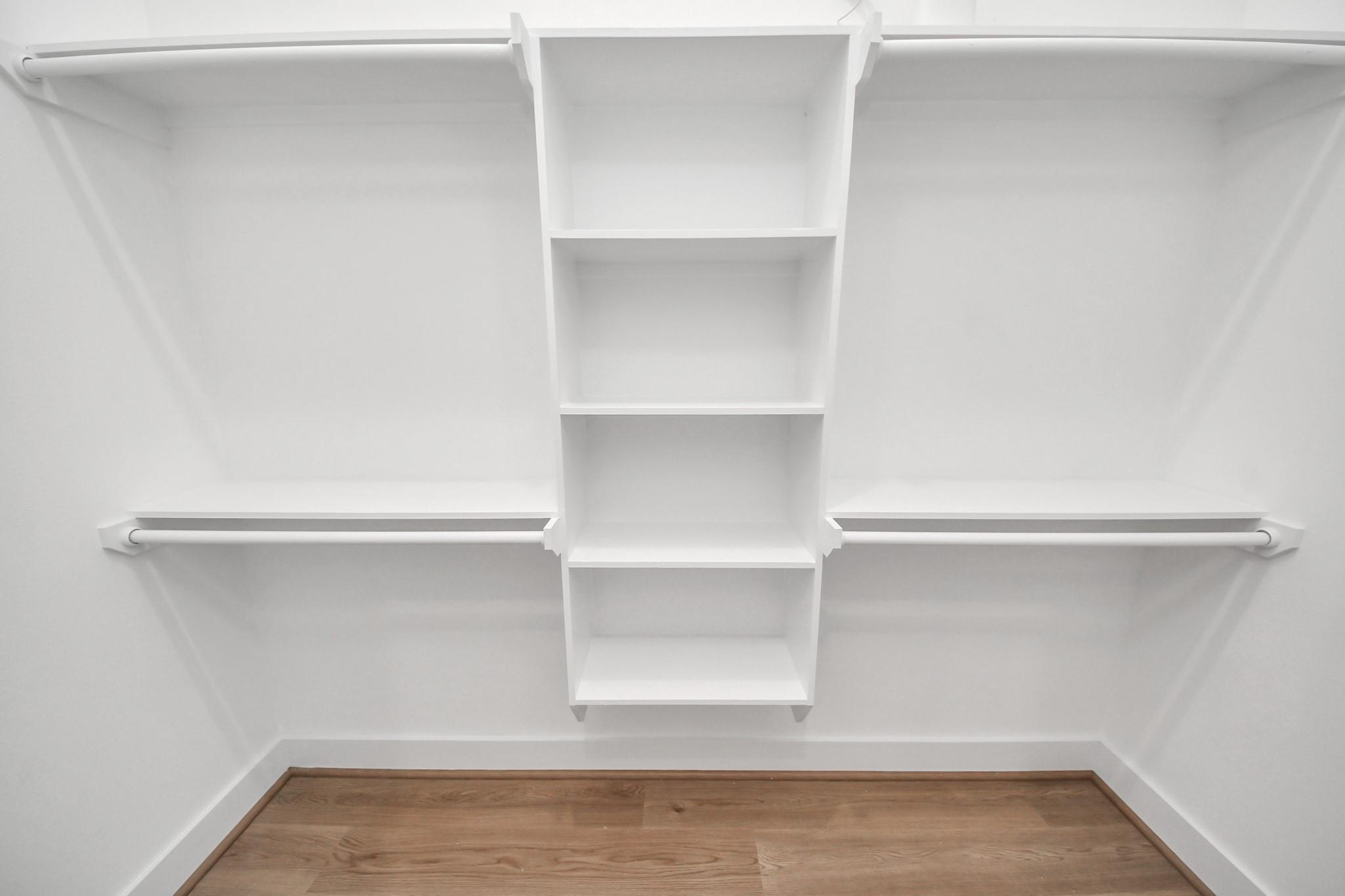 Empty closet with central built-in shelves, hanging rods, and a wood plank floor.