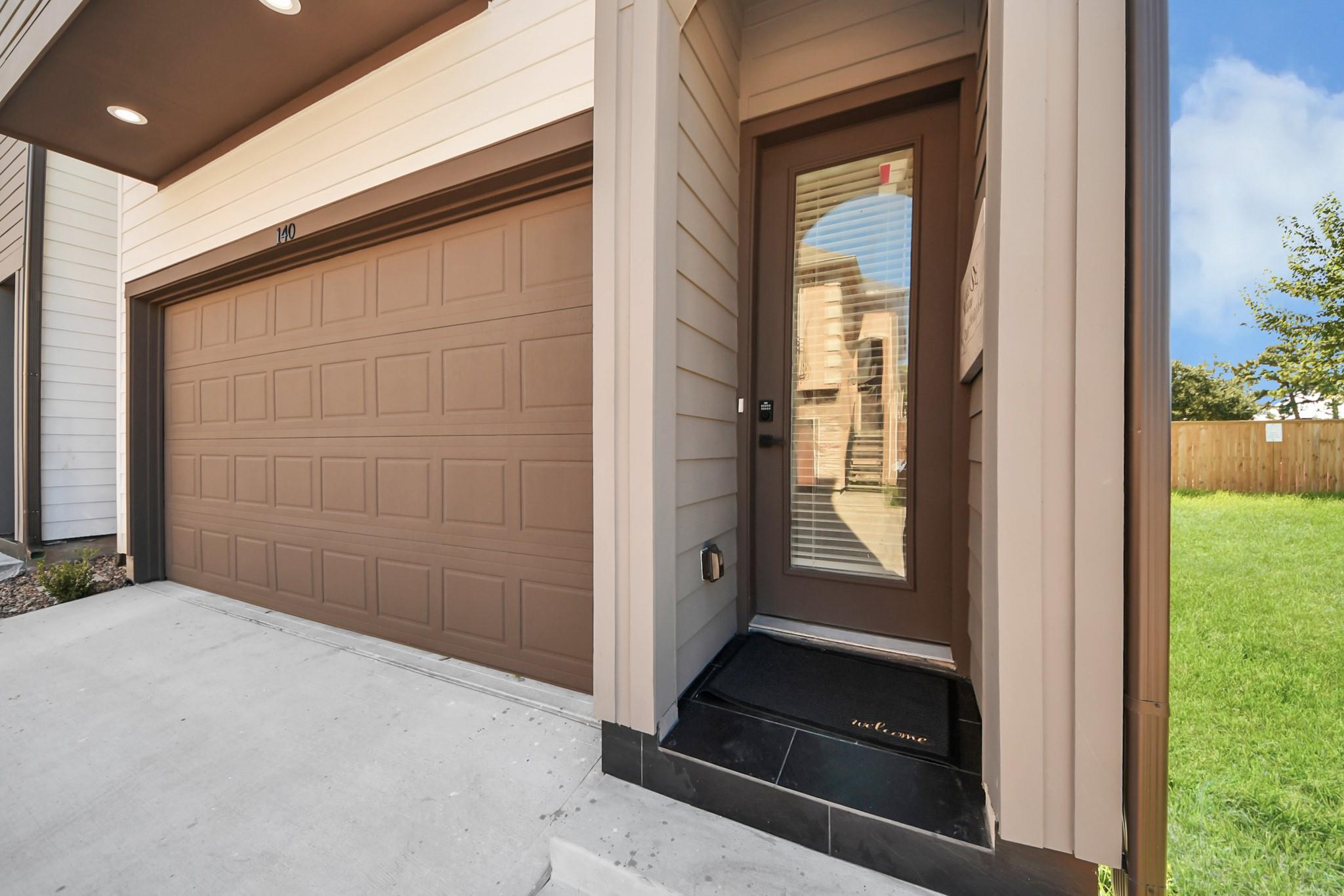Home entrance beside a brown paneled garage door, with a glass-panel door and keypad.