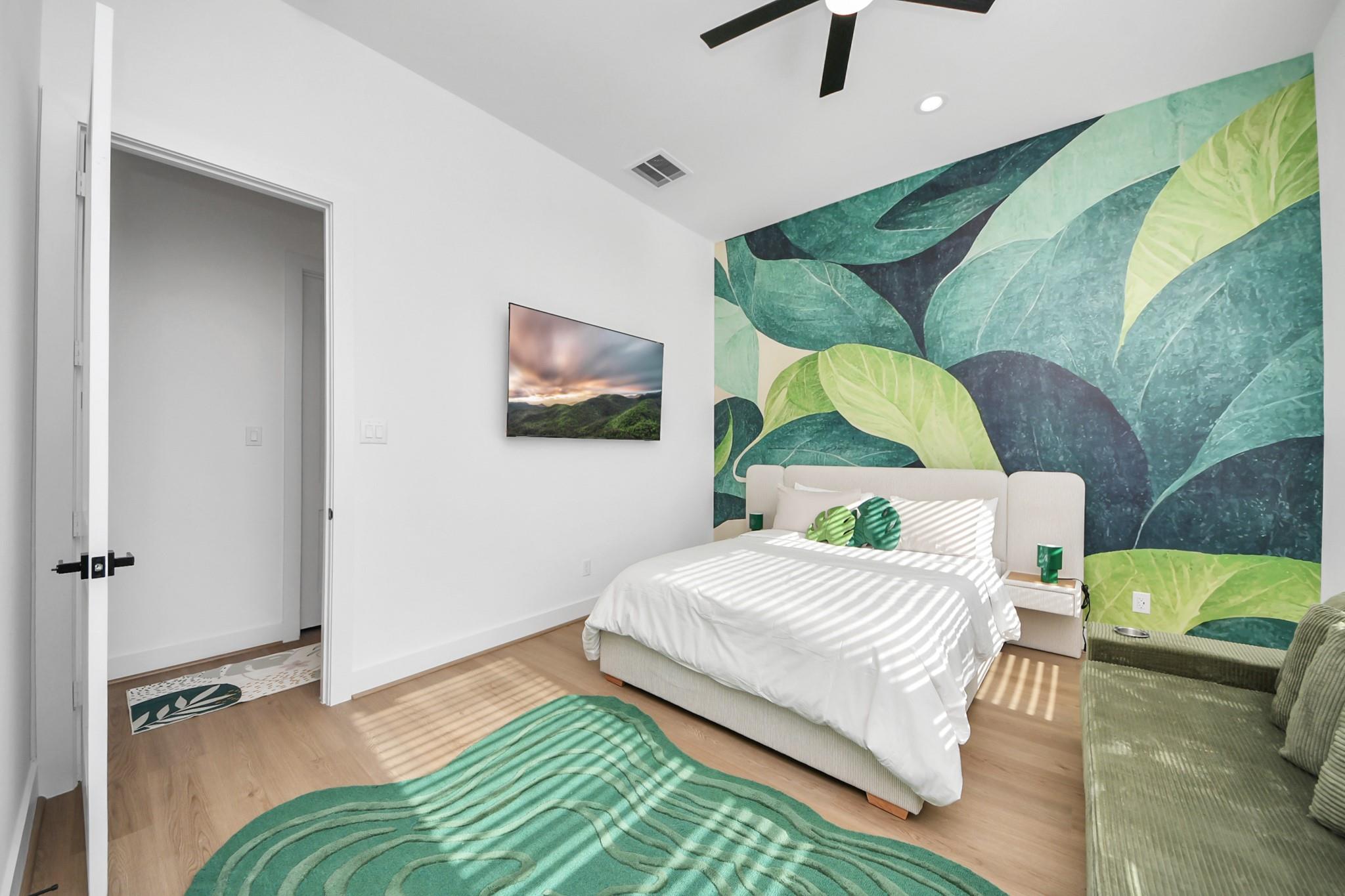 Bedroom with a white bed beneath a large green leaf mural and a green sofa.