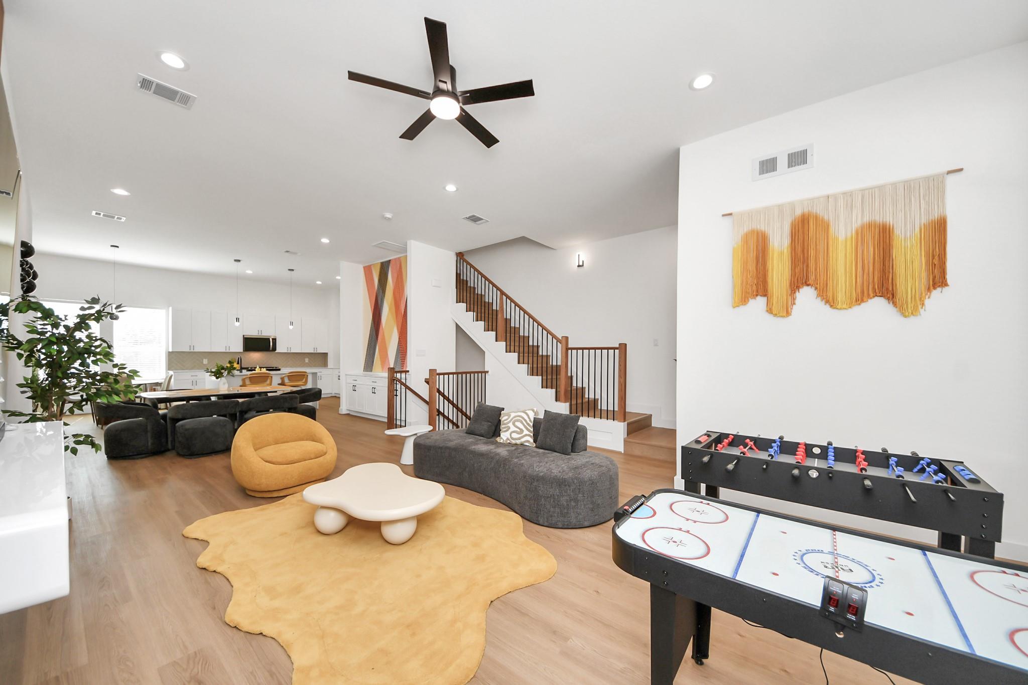 Open-plan living room with staircase, kitchen, and air hockey and foosball tables.