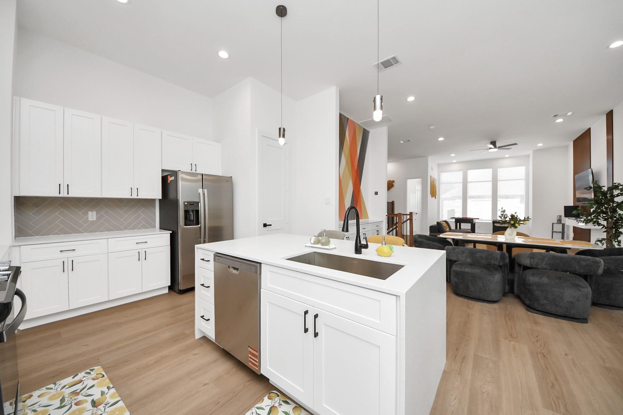 Open-plan kitchen with a large white island, black faucet, and stainless steel appliances beside a furnished living area.