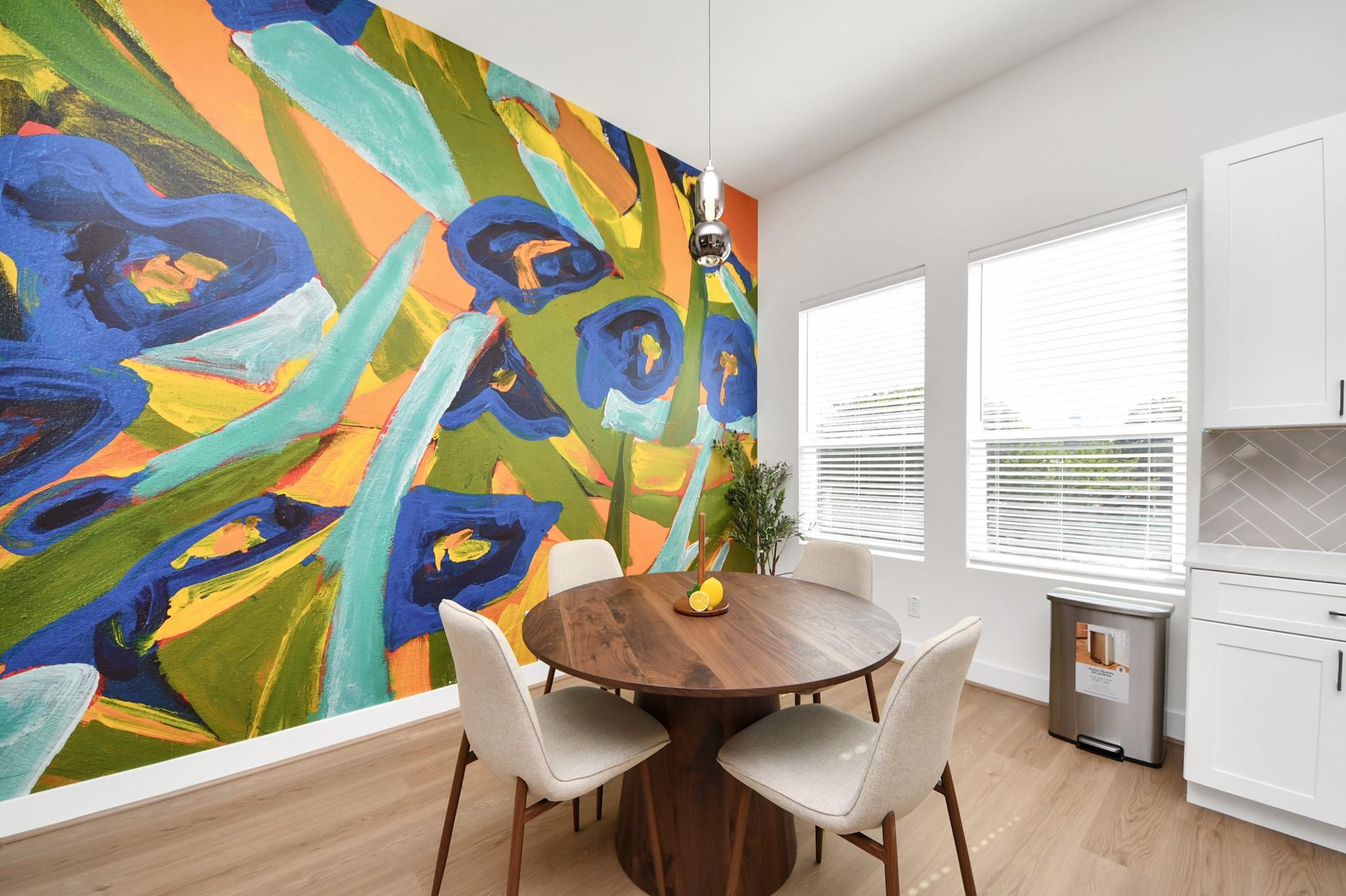 Dining area with a round wooden table, white cabinetry, and a vivid abstract mural.