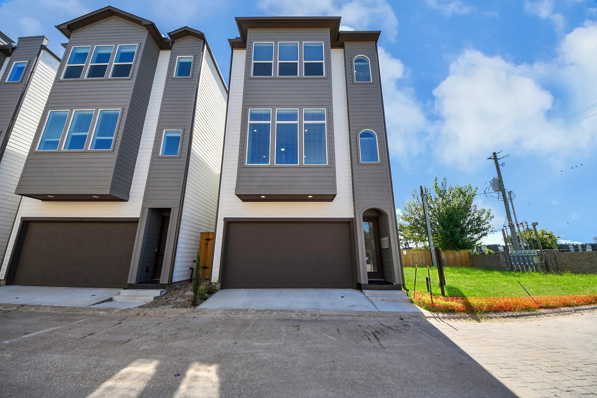 Modern gray townhouse with a two-car garage and tall windows beside a grassy lot.