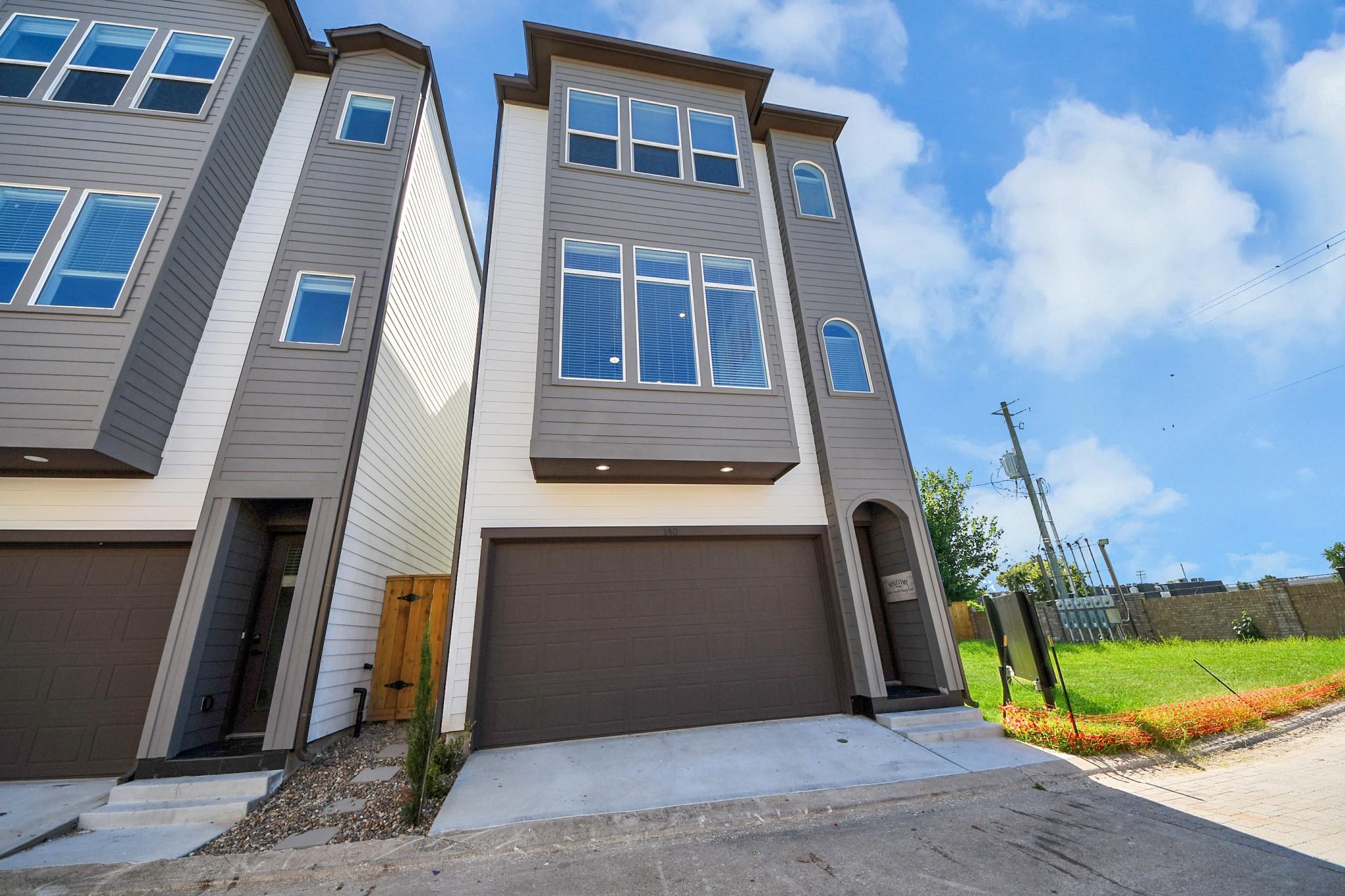 Multi-story gray townhouse with a large attached garage and arched entry.