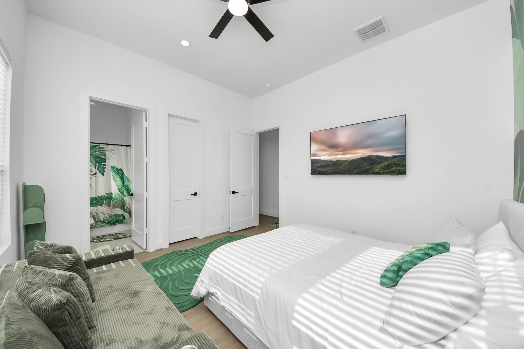 Bright bedroom with a white bed, green patterned rug, and gray ribbed armchair.