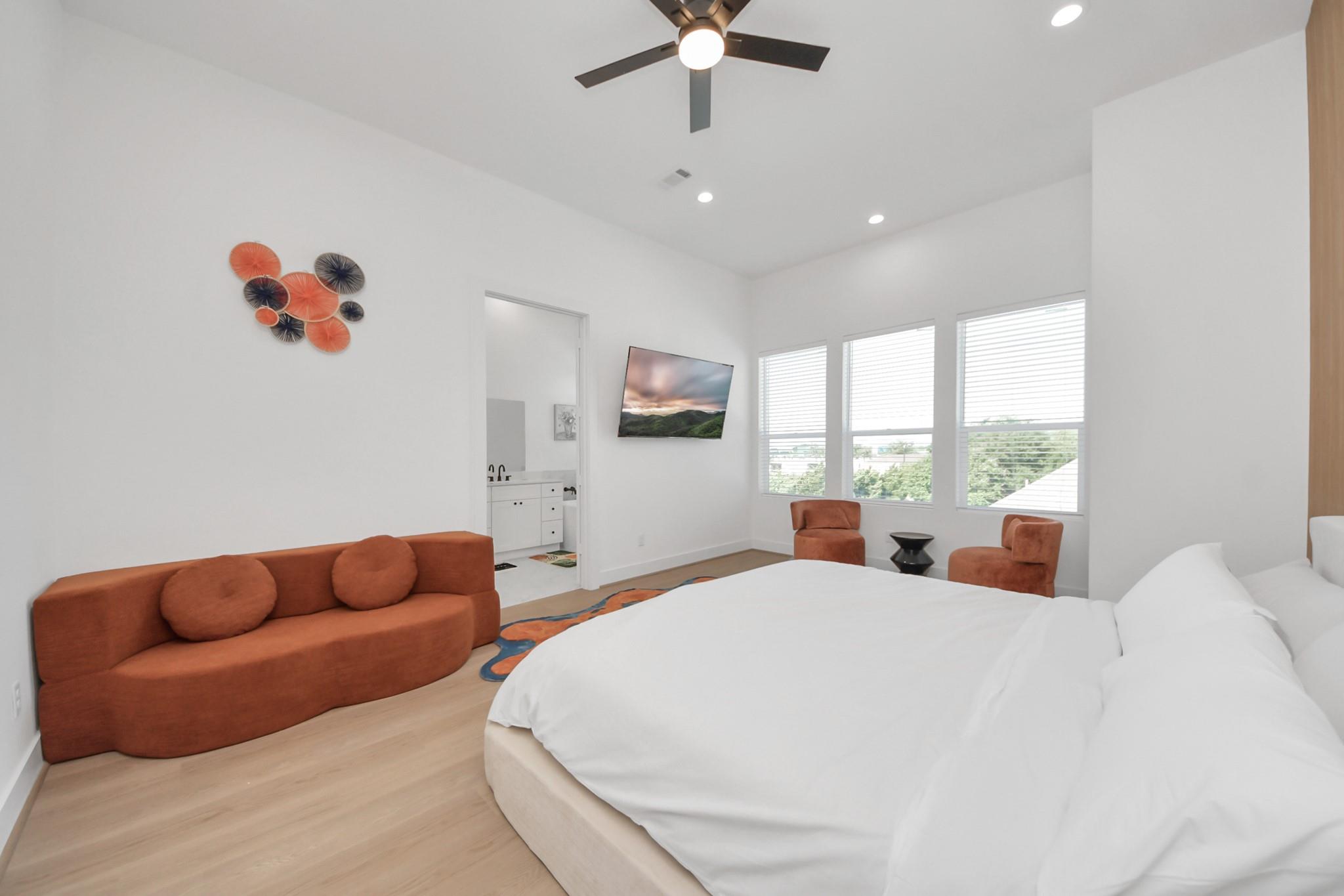 Bright bedroom with a white bed, rust-colored seating, and three windows.