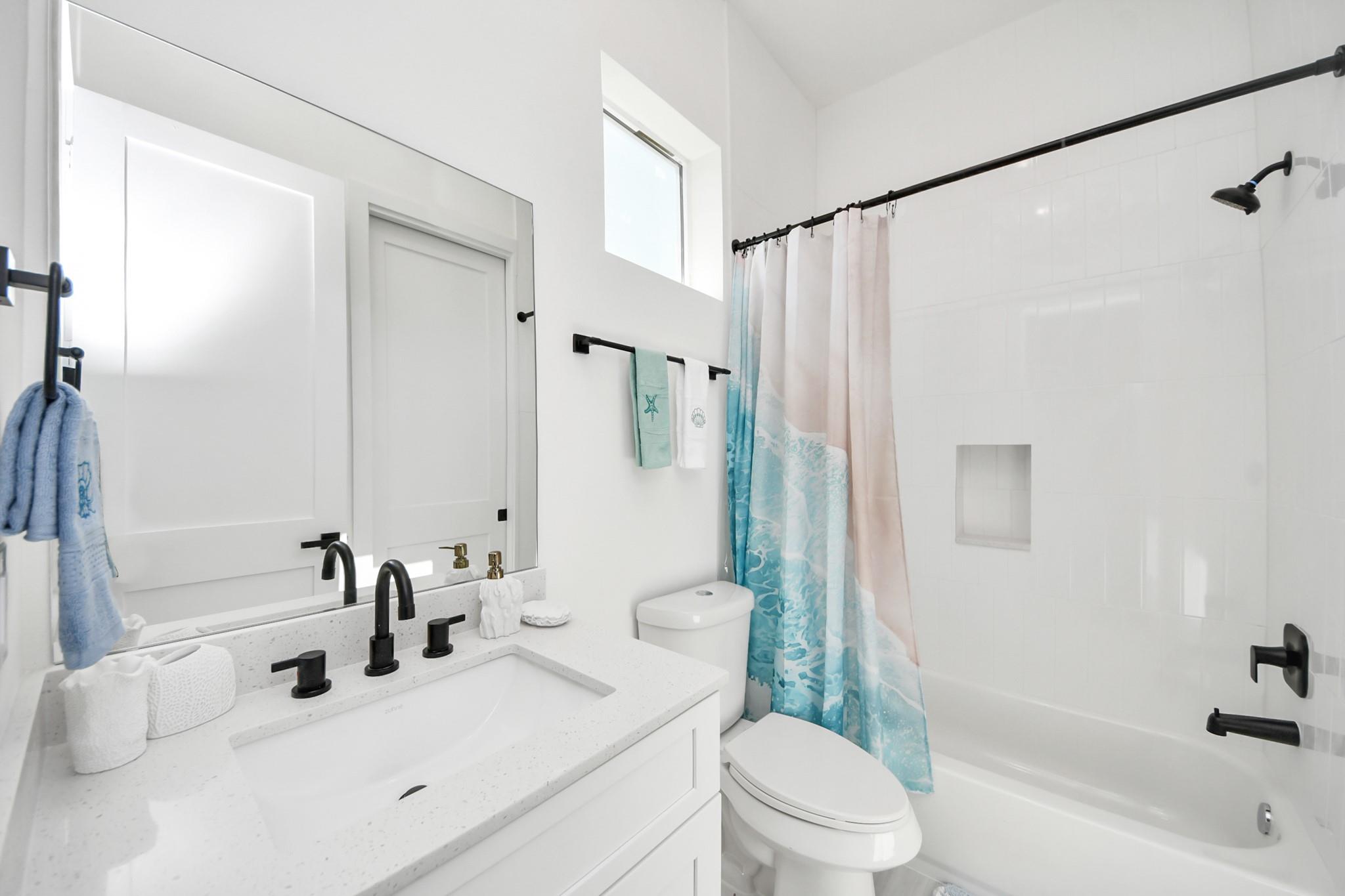 Bright white bathroom with a speckled vanity, black fixtures, and a blue-and-pink shower curtain.