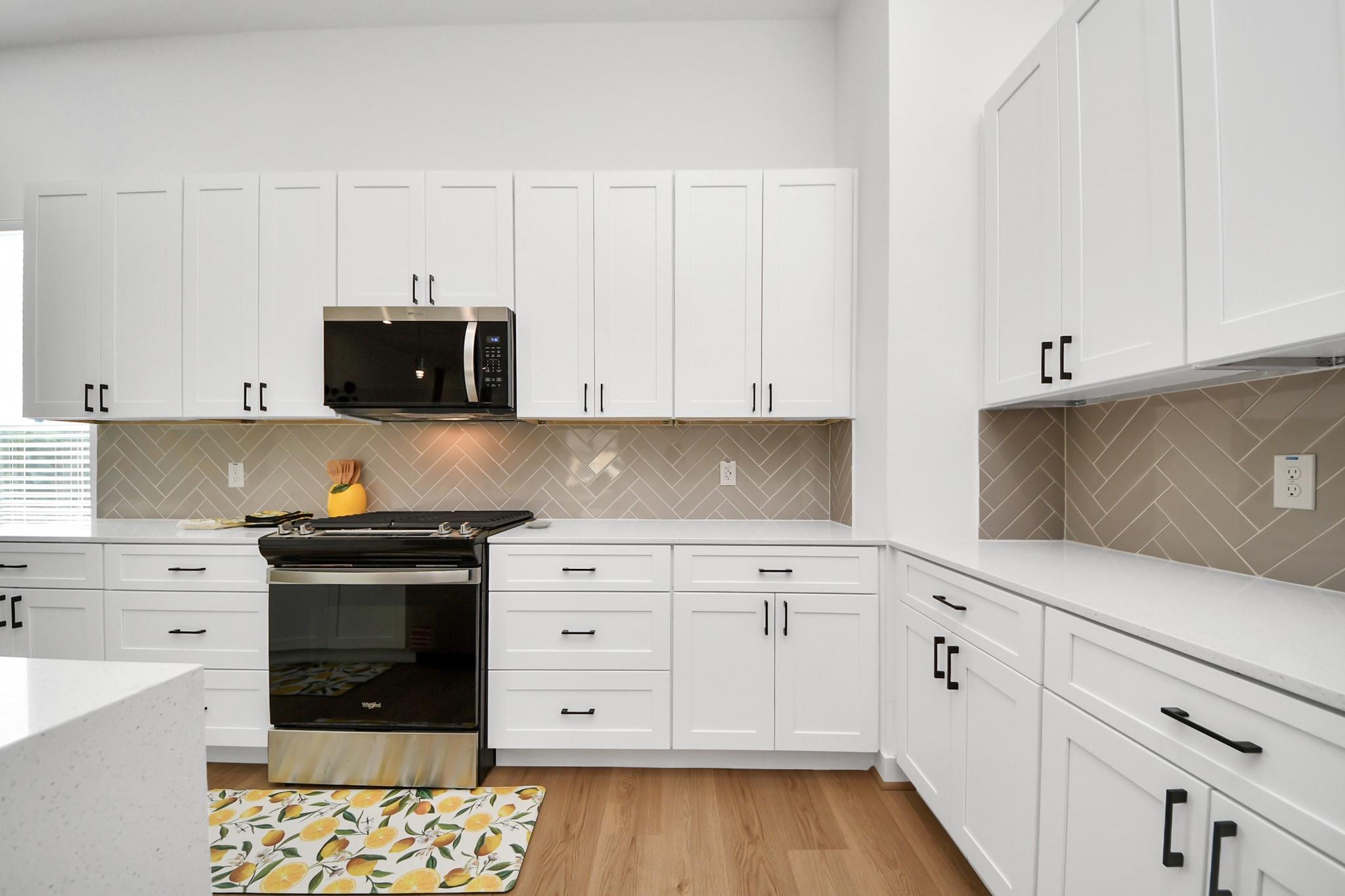 Kitchen with white shaker cabinets, taupe diagonal tile backsplash, and black range.