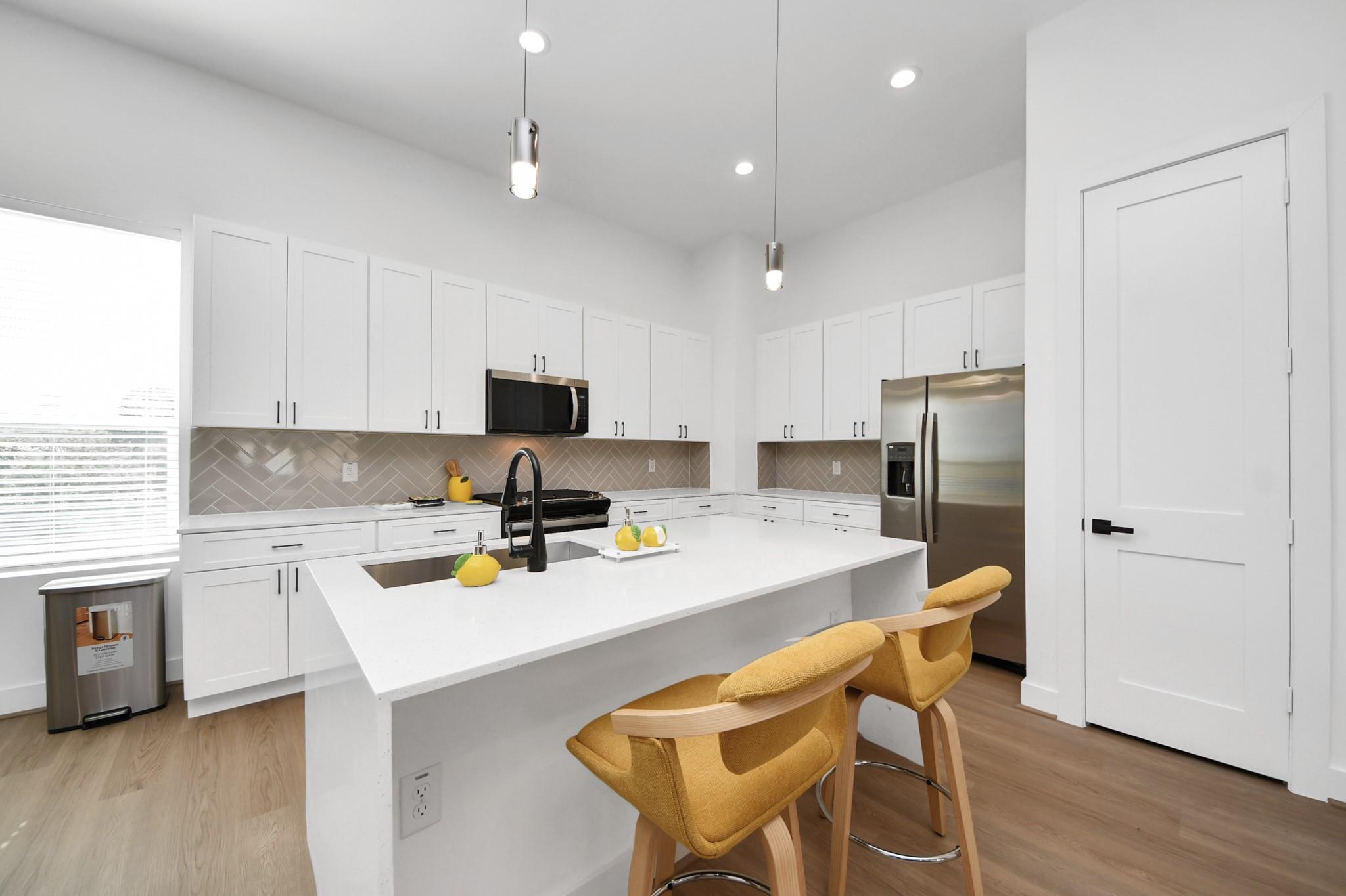 Modern white kitchen with a large island, herringbone backsplash, stainless appliances, and mustard-yellow bar stools.