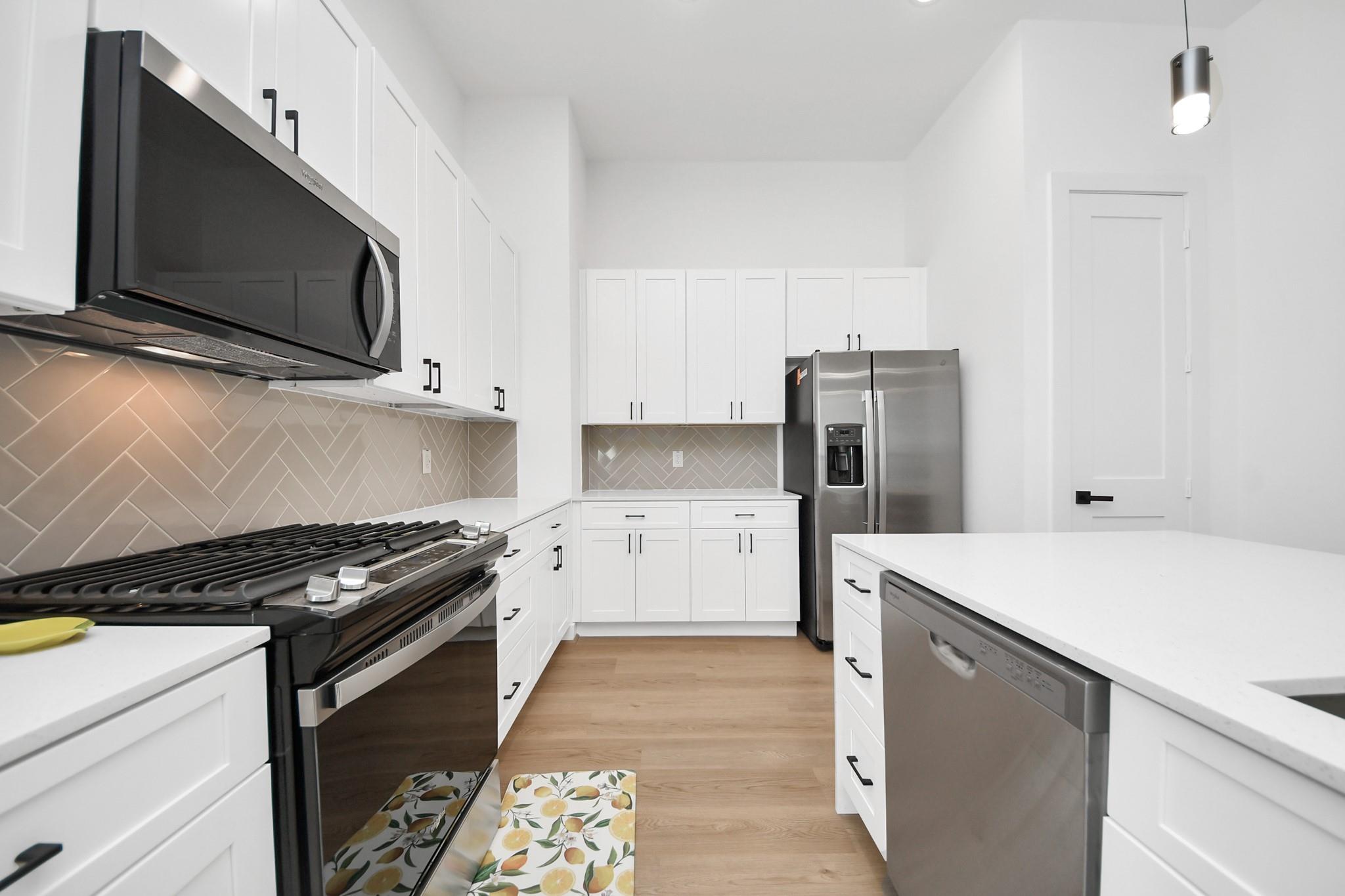 Modern kitchen with white cabinets, herringbone tile backsplash, black range, and stainless steel appliances.