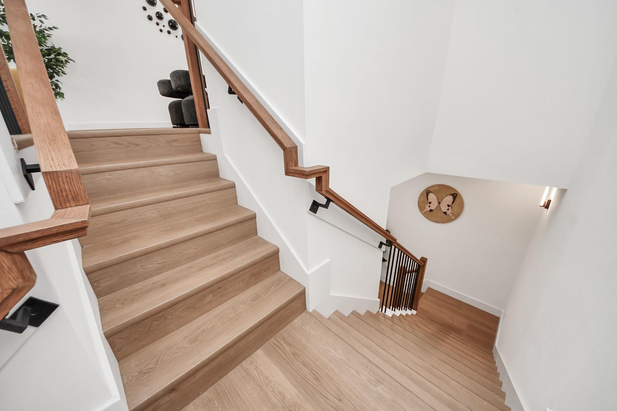 Multi-level staircase with light wood treads, wood handrails, and black metal balusters.