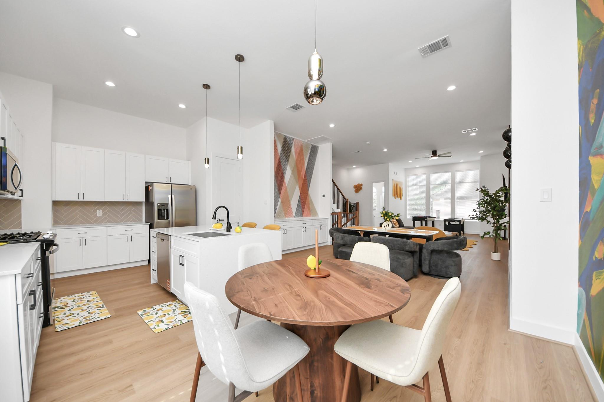 Open-plan kitchen and living area with a large white island, round dining table, and geometric accent wall.