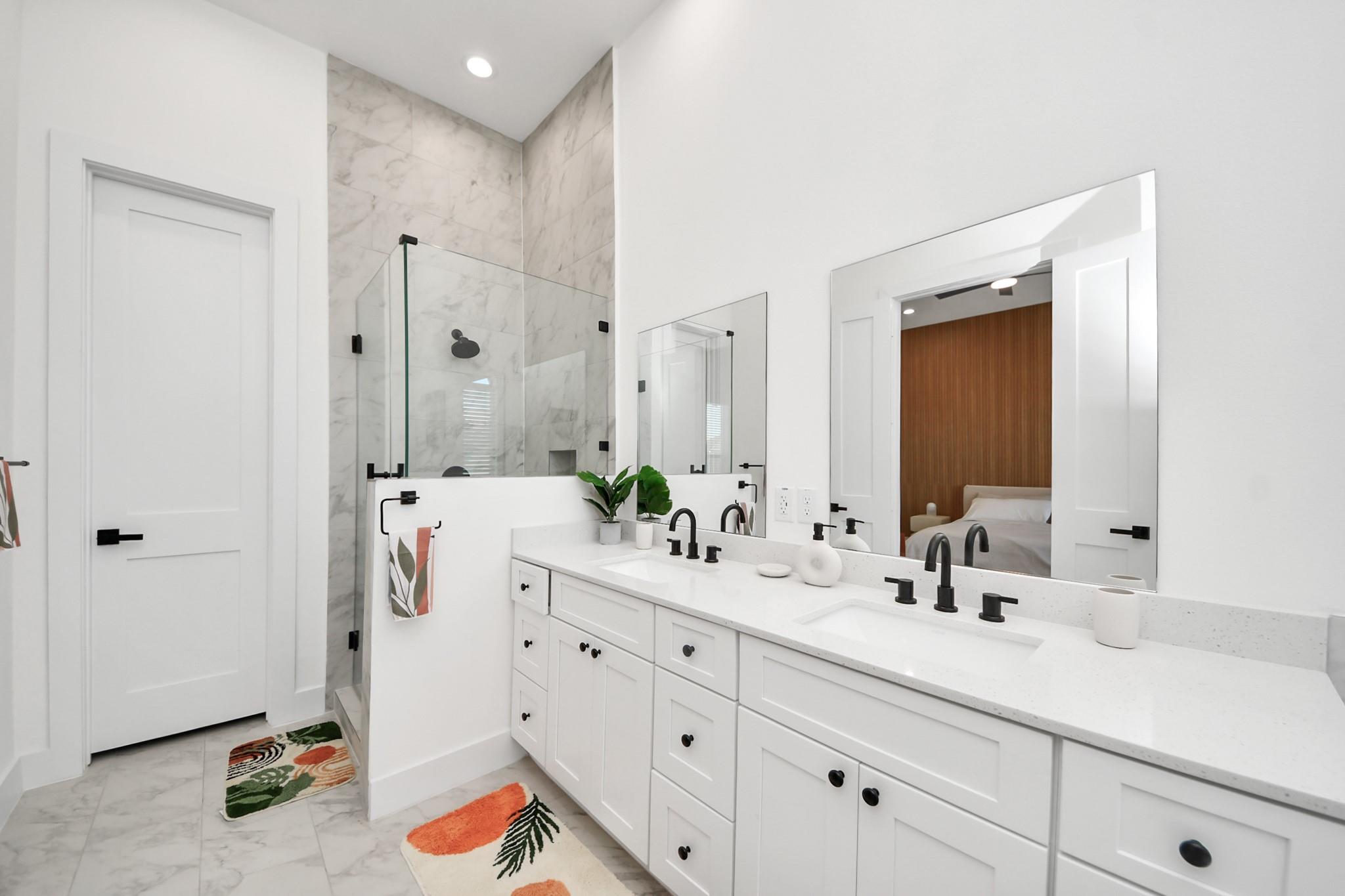 Staged bathroom with a double vanity and a glass shower lined with marble-look tile.