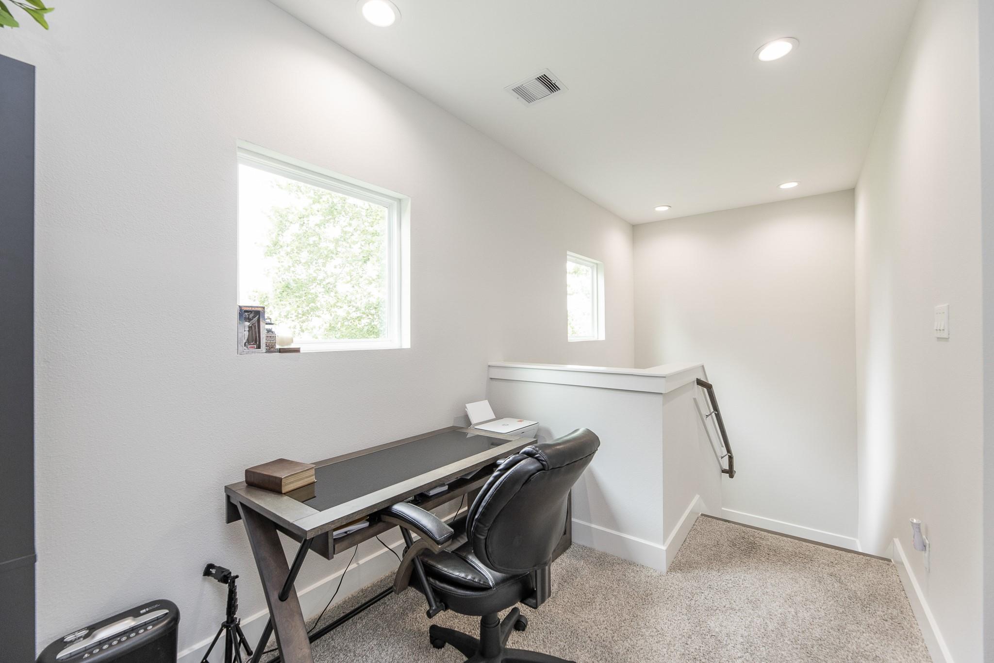 Carpeted home office with a dark desk, black chair, and two windows.