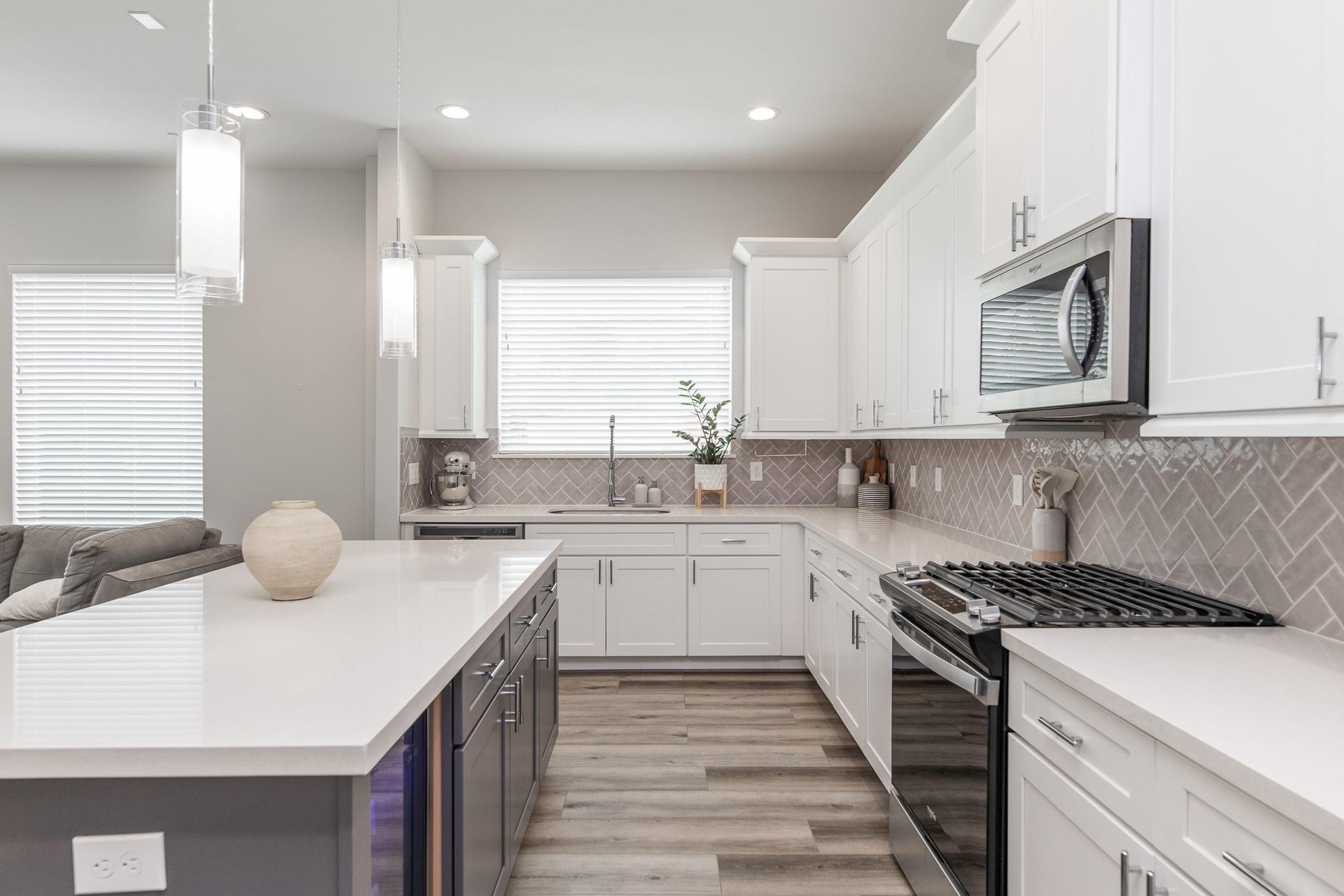Bright kitchen with a large island, white cabinets, herringbone backsplash, and stainless steel gas range.