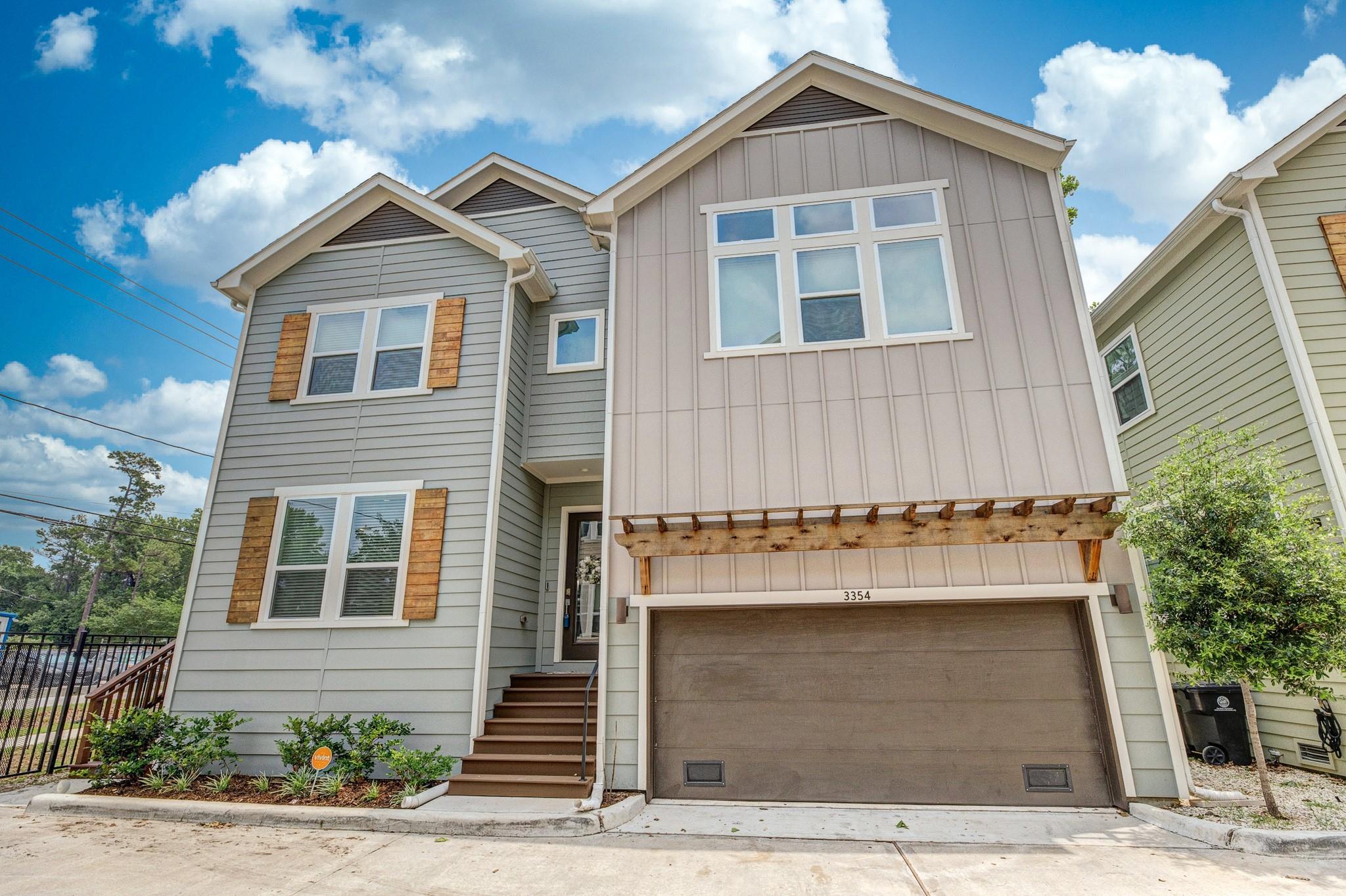 Multi-story gray home with a two-car garage, wooden pergola, and front steps.