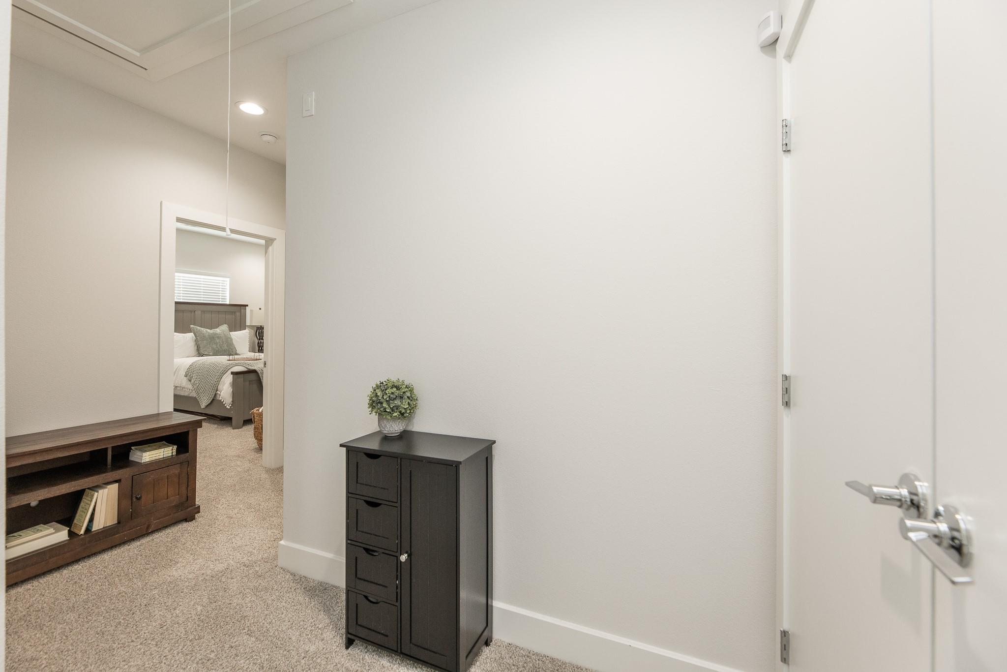 Carpeted hallway with a dark cabinet and an open doorway to a staged bedroom.