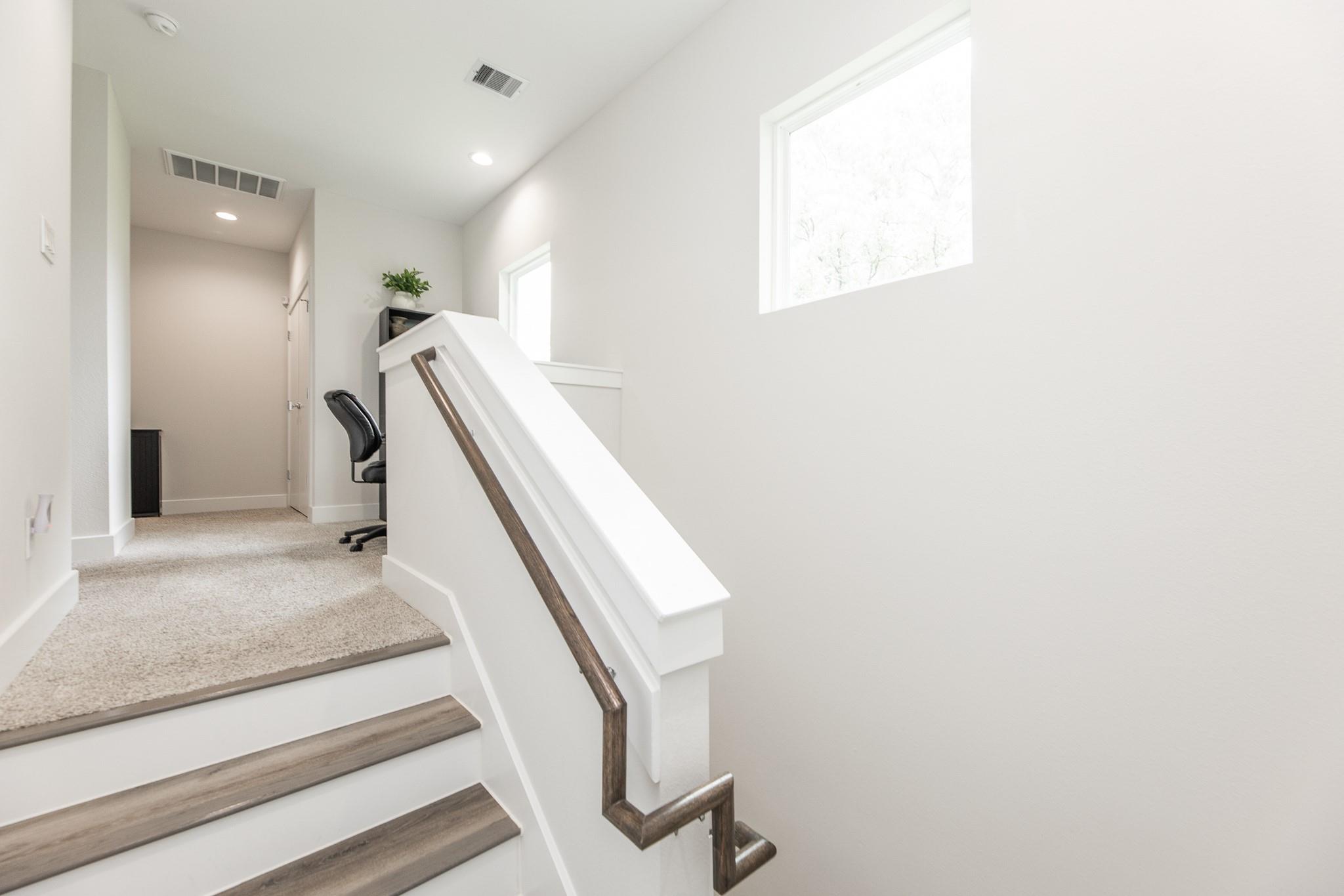 Interior staircase with wood-look treads, a dark handrail, and a carpeted upper landing.